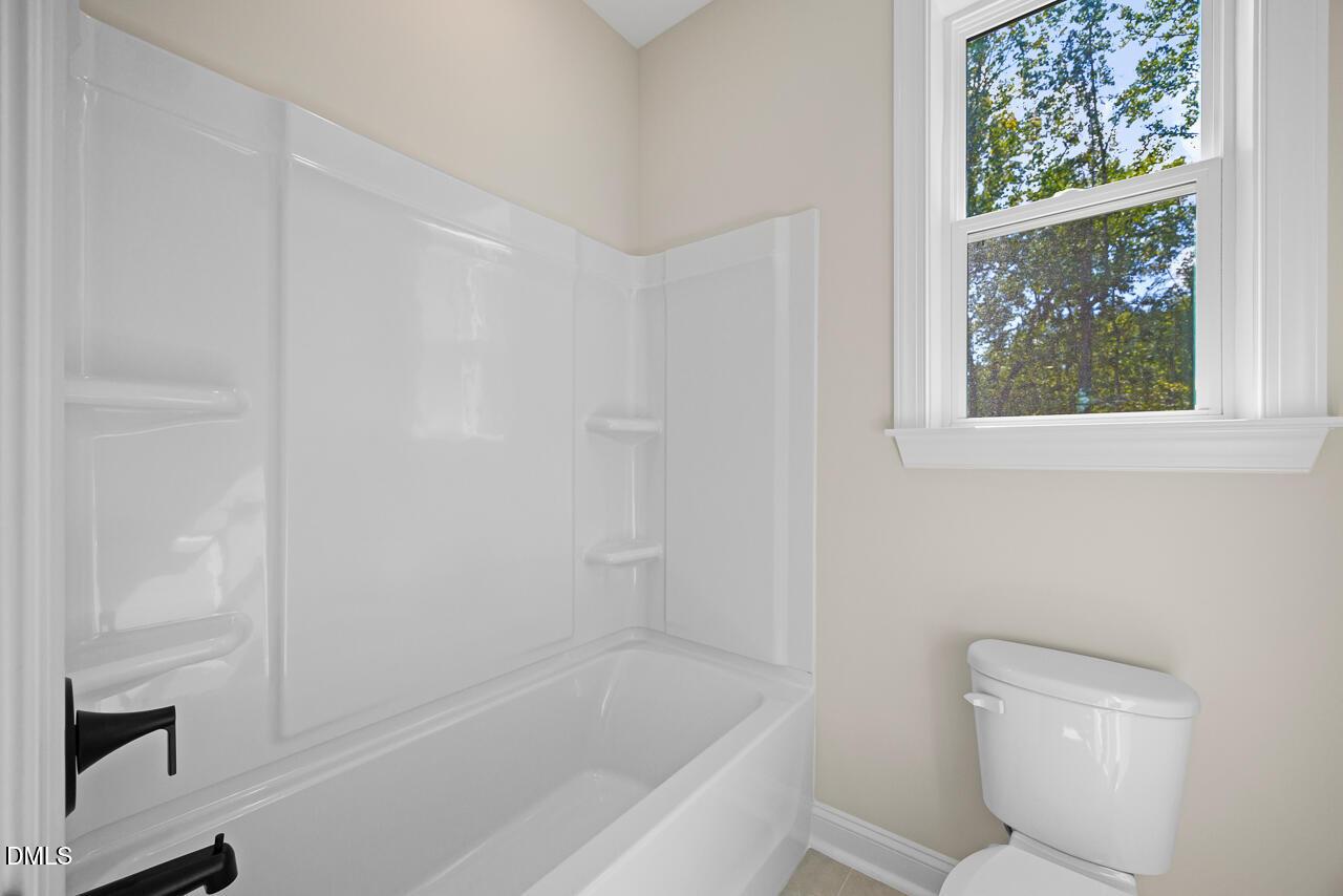Bright white bathtub with black fixtures beside toilet and window in Davidson Homes The Crawford D bathroom, Wake Forest, NC
