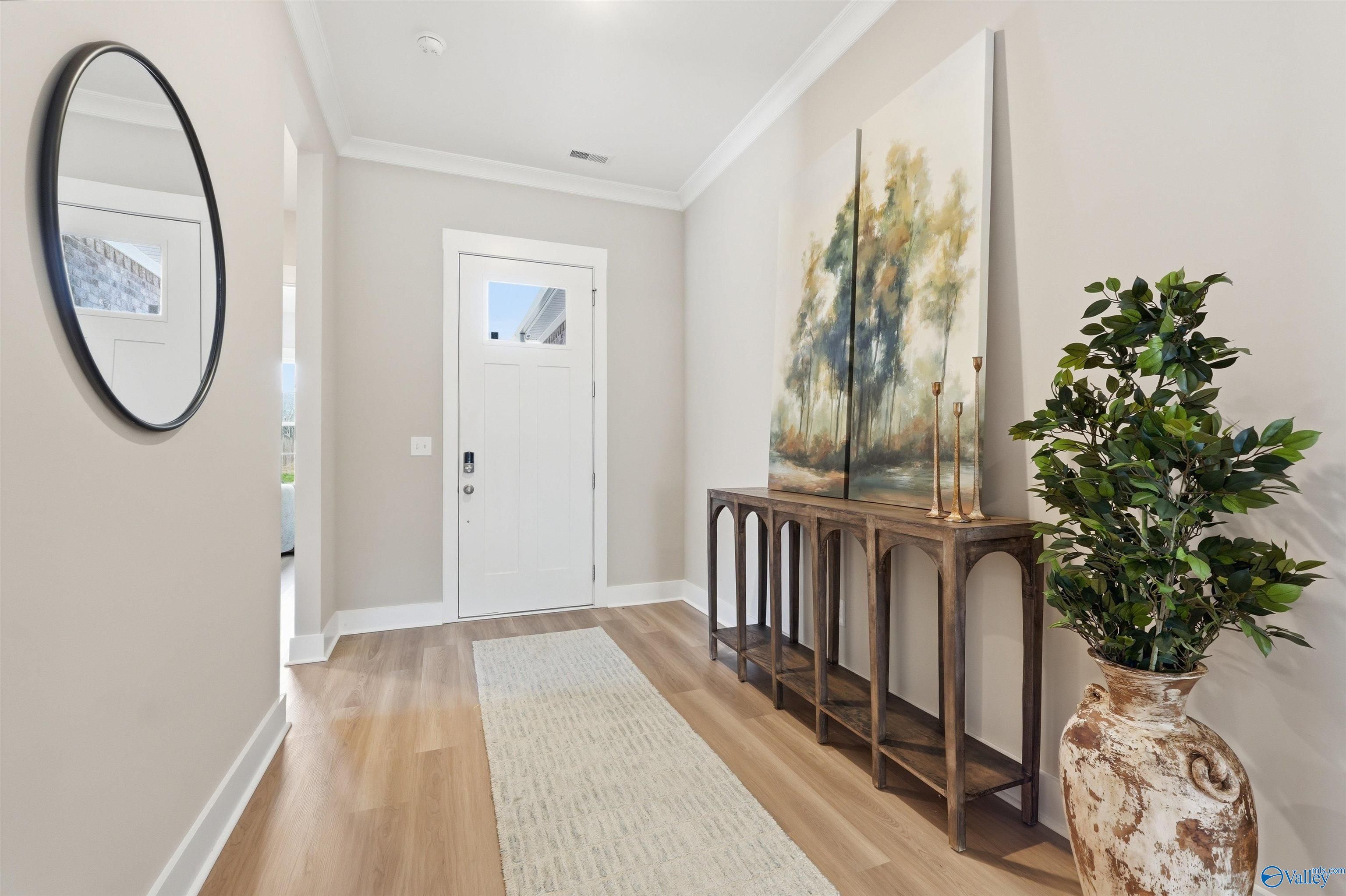 Elegant foyer with round mirror, white entry door, wooden console table, abstract tree painting, and potted plant in Evermore Homes Oxford B, Owens Cross Roads AL