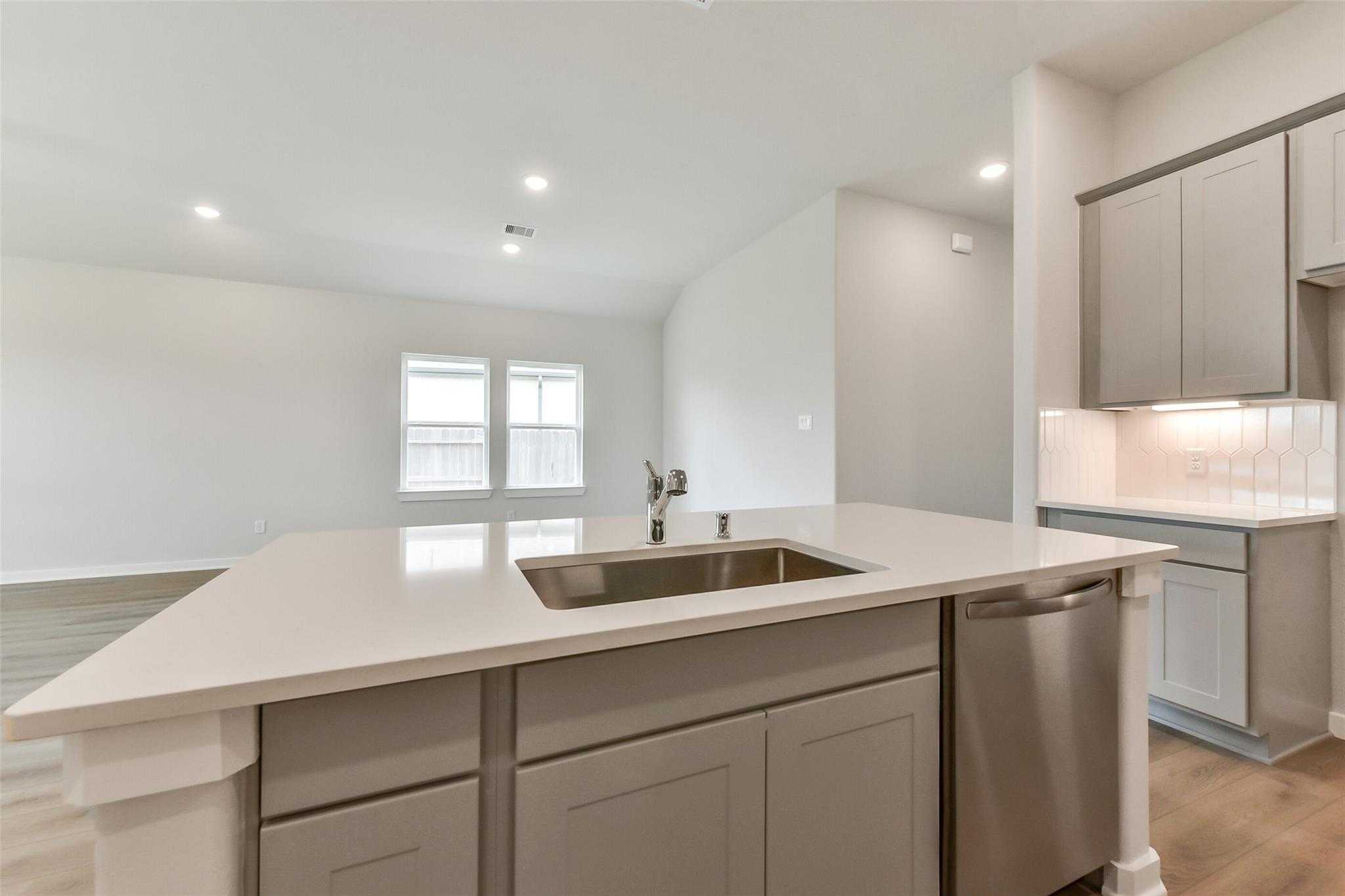 Modern kitchen island with white quartz counters, stainless sink, dishwasher, and gray cabinets in Davidson Homes The Laguna C, Rosharon, Texas