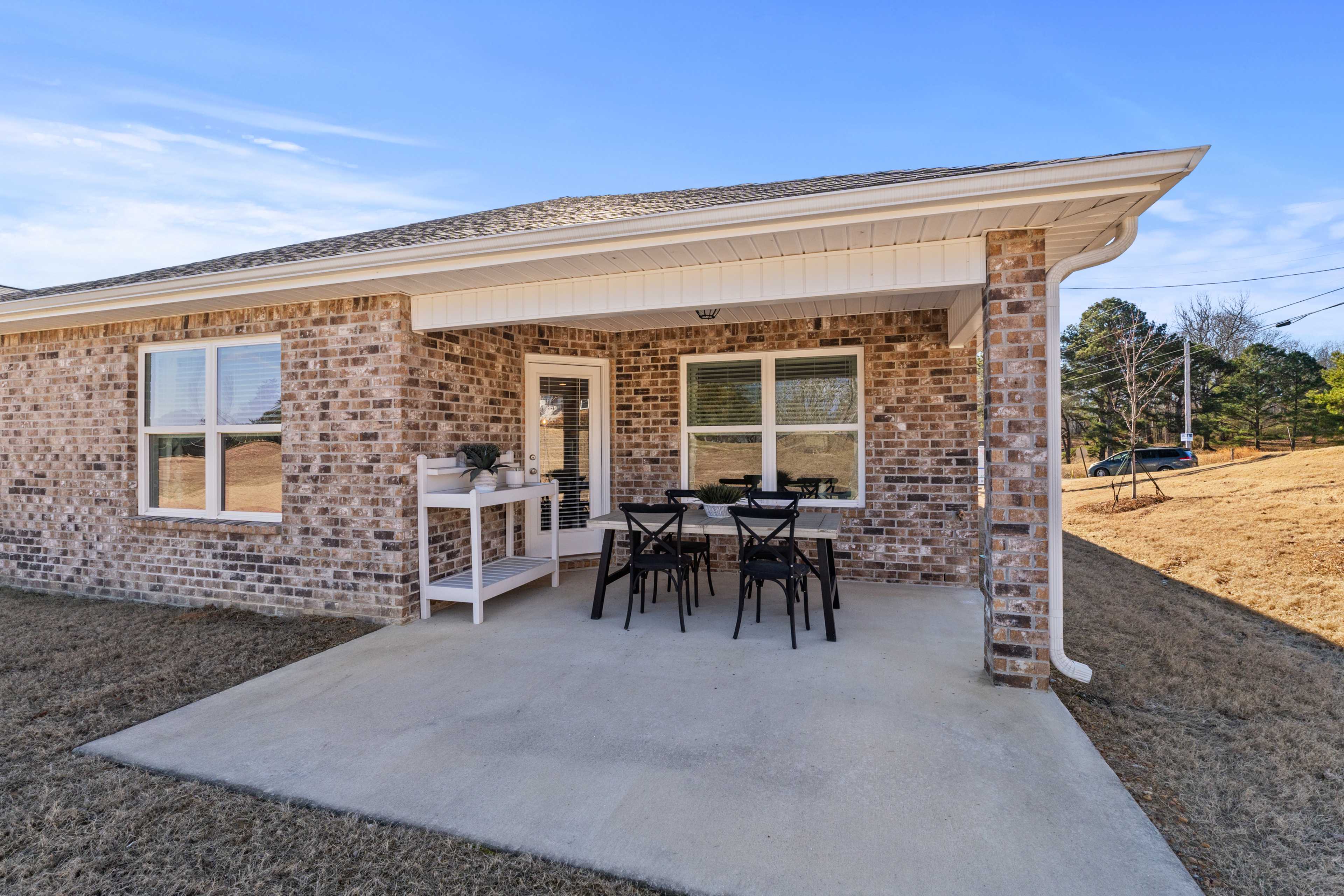 Brick home covered patio with black metal dining set and potted plants at Ramsay Cove in Owens Cross Roads, Alabama