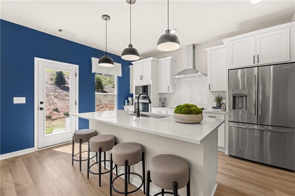 Modern kitchen with white cabinets, stainless appliances, island bar stools, and blue accent wall door to backyard in Davidson Homes The Burton C, Canton GA