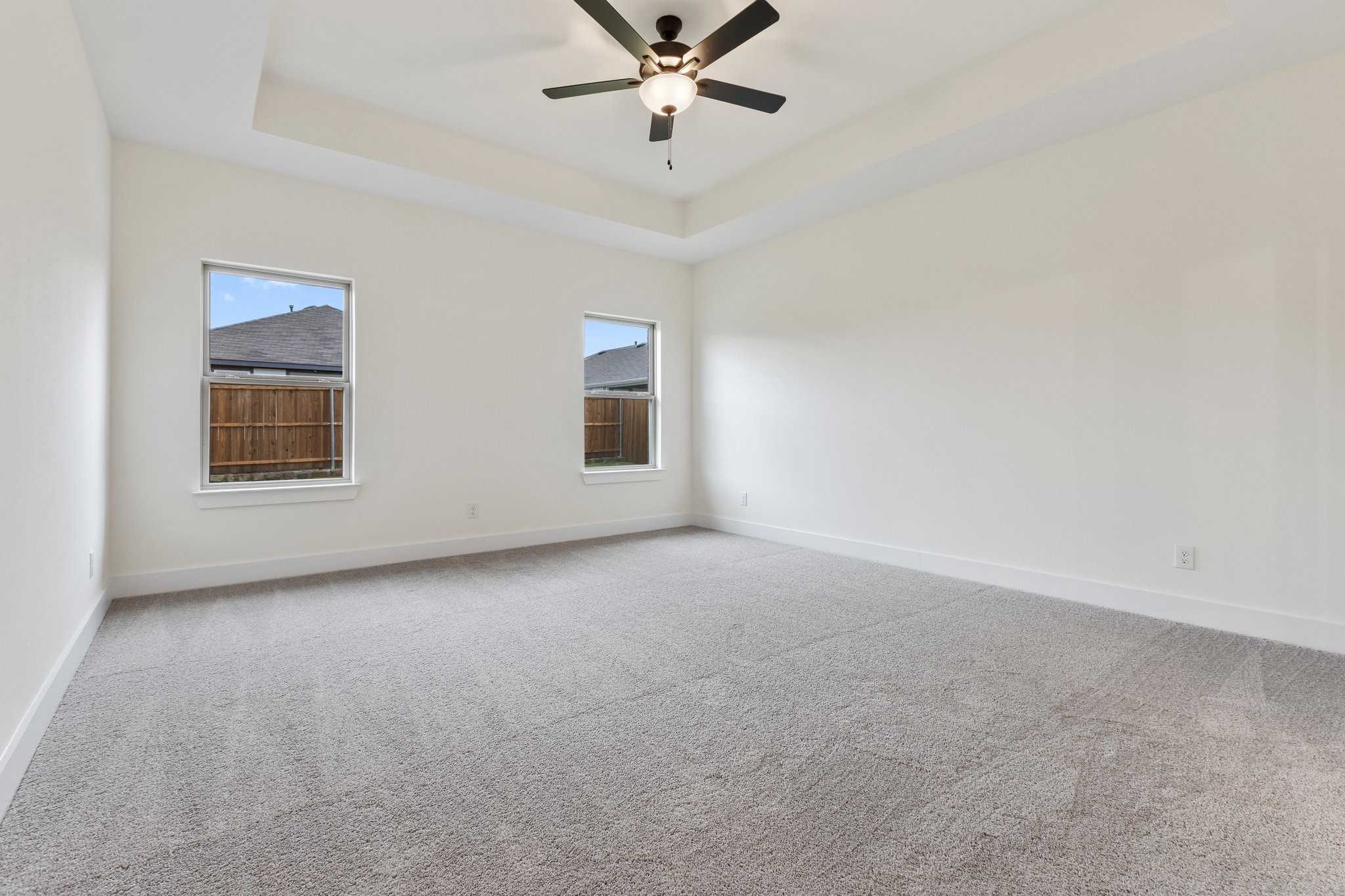 Spacious empty bedroom with tray ceiling, ceiling fan, carpeted floor, and windows in Davidson Homes The Rockford C, Josephine, Texas