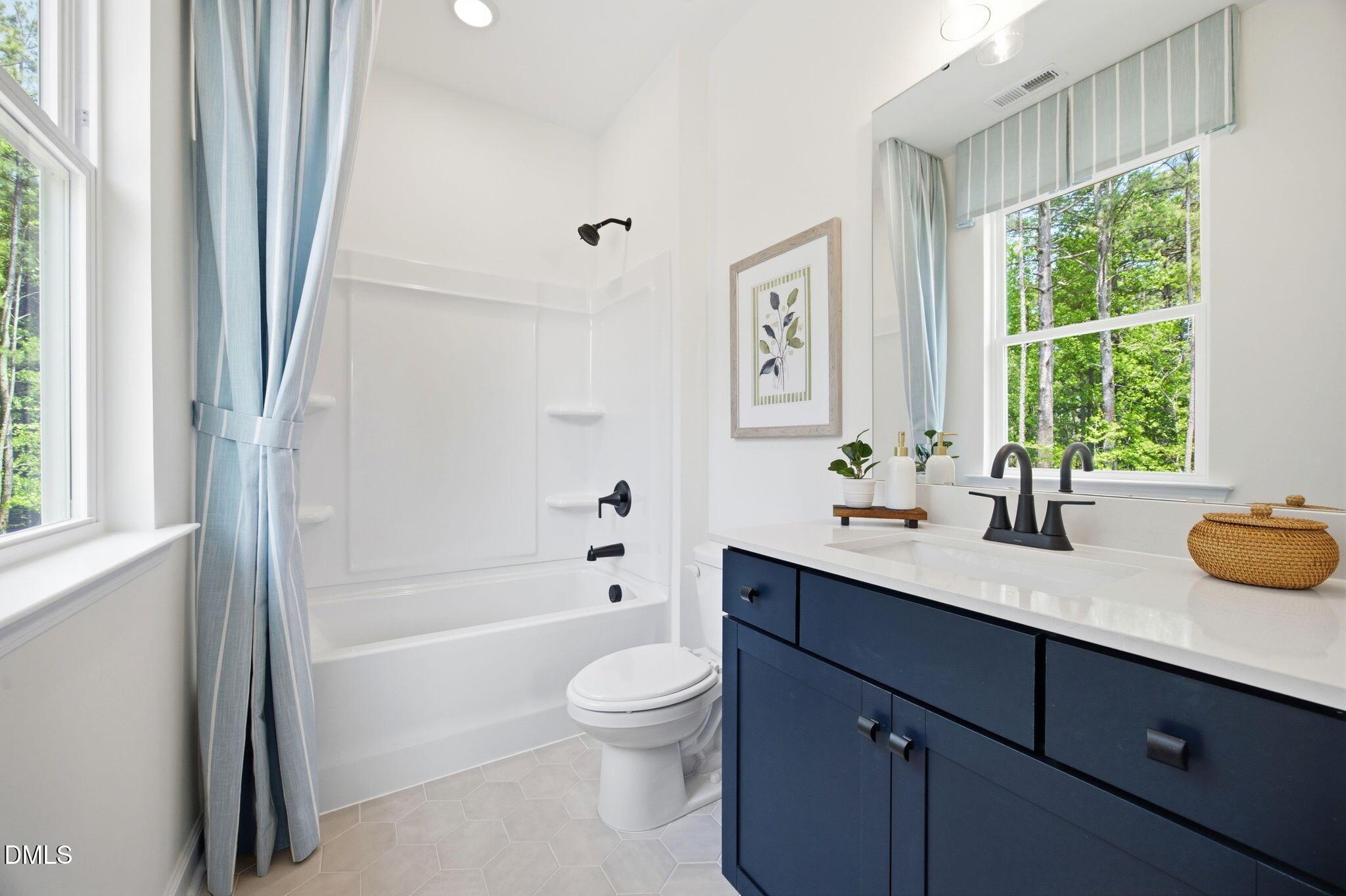 Modern bathroom with navy blue vanity, tub-shower combo, and tiled floor in The Ashport M at Wendell Ridge, North Carolina.