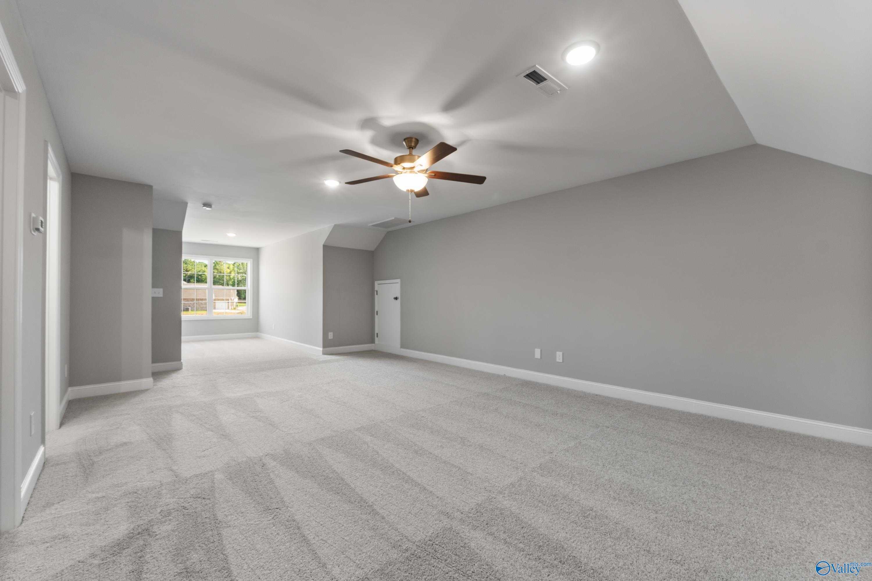 Spacious vaulted-ceiling room with gray carpet, ceiling fan, and large window in Davidson Homes The Rockford, Harvest, Alabama