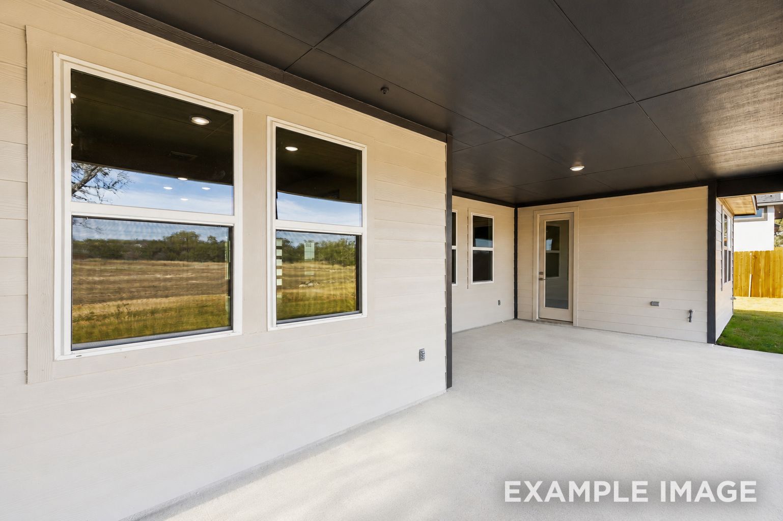 Covered back patio of The Oxford home design featuring light siding, recessed lighting, and expansive backyard views.