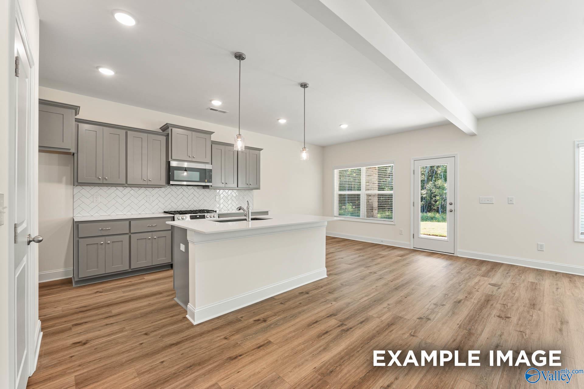 Modern open kitchen with gray shaker cabinets, subway tile backsplash, stainless appliances, and large white island in The Shelby A, Hazel Green, AL