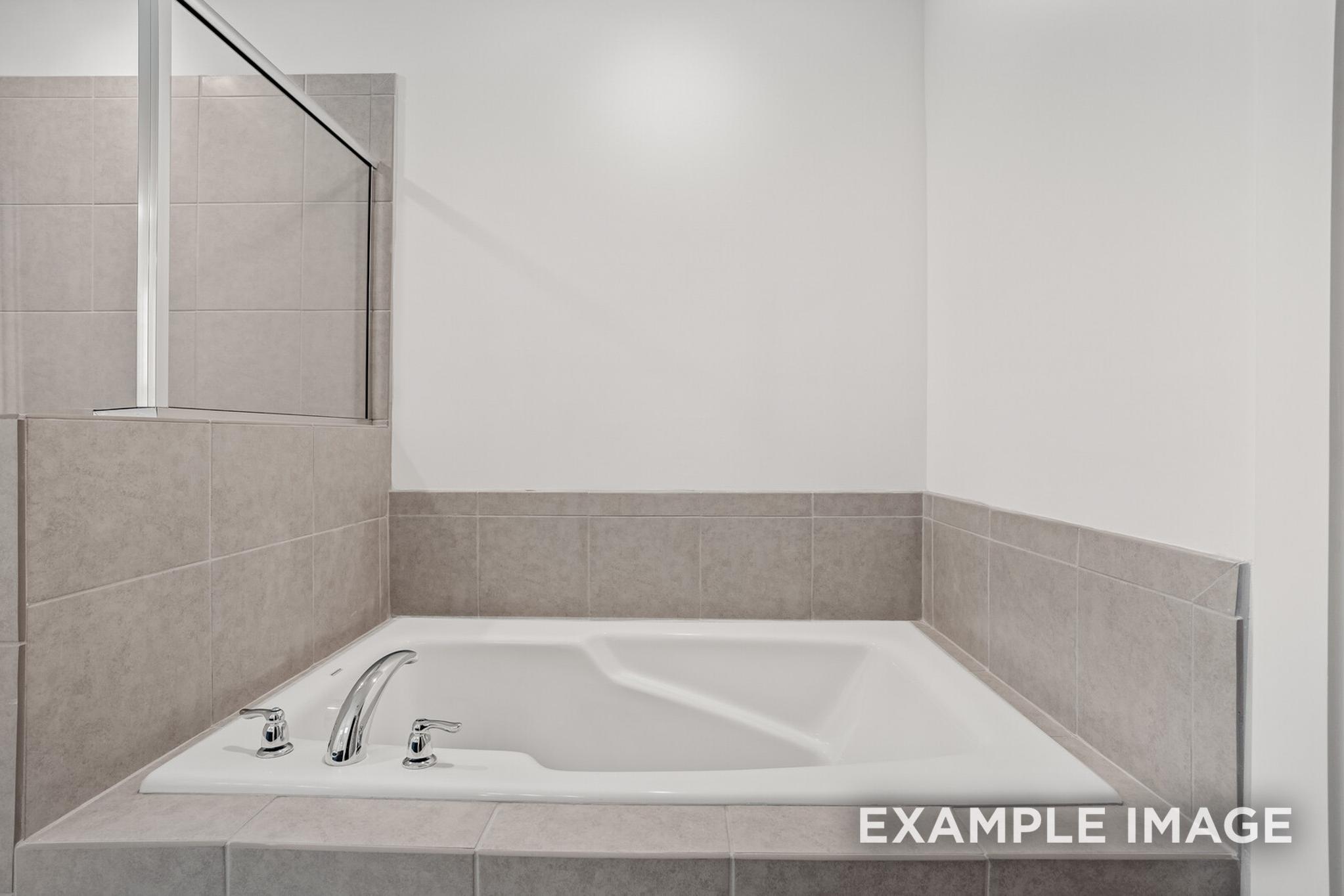 Spacious master bathroom in The Logan C with gray tile surround, soaking tub, and glass shower enclosure