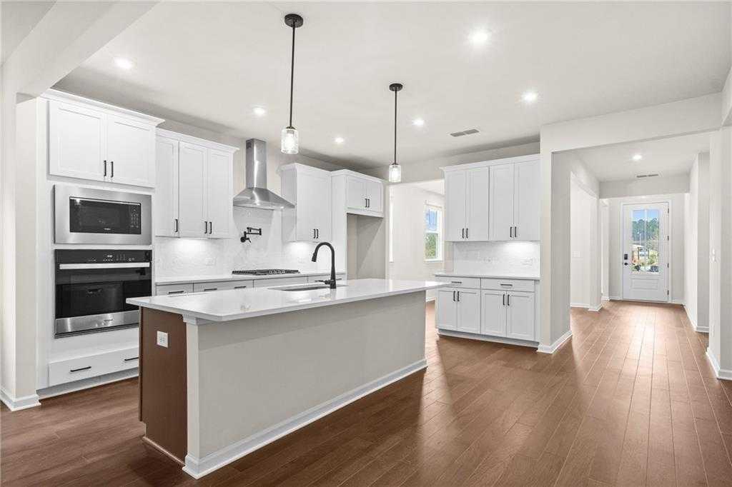 Modern white kitchen with stainless double ovens, quartz island, and pendant lights in Davidson Homes The Glenwood C, Loganville, GA