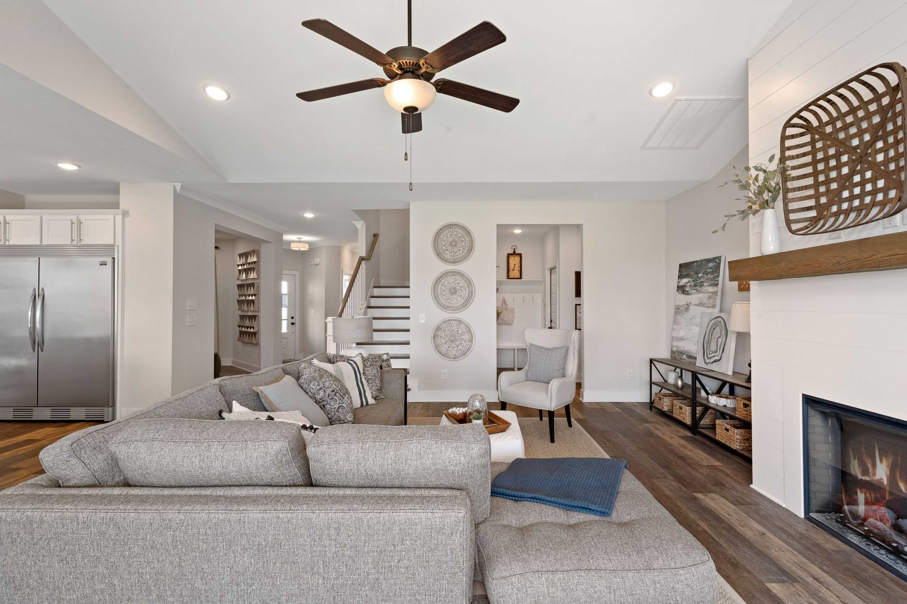 Spacious open-concept living room in Rivers Edge Murfreesboro TN with gray L-shaped sofa, gas fireplace, hardwood floors, and ceiling fan