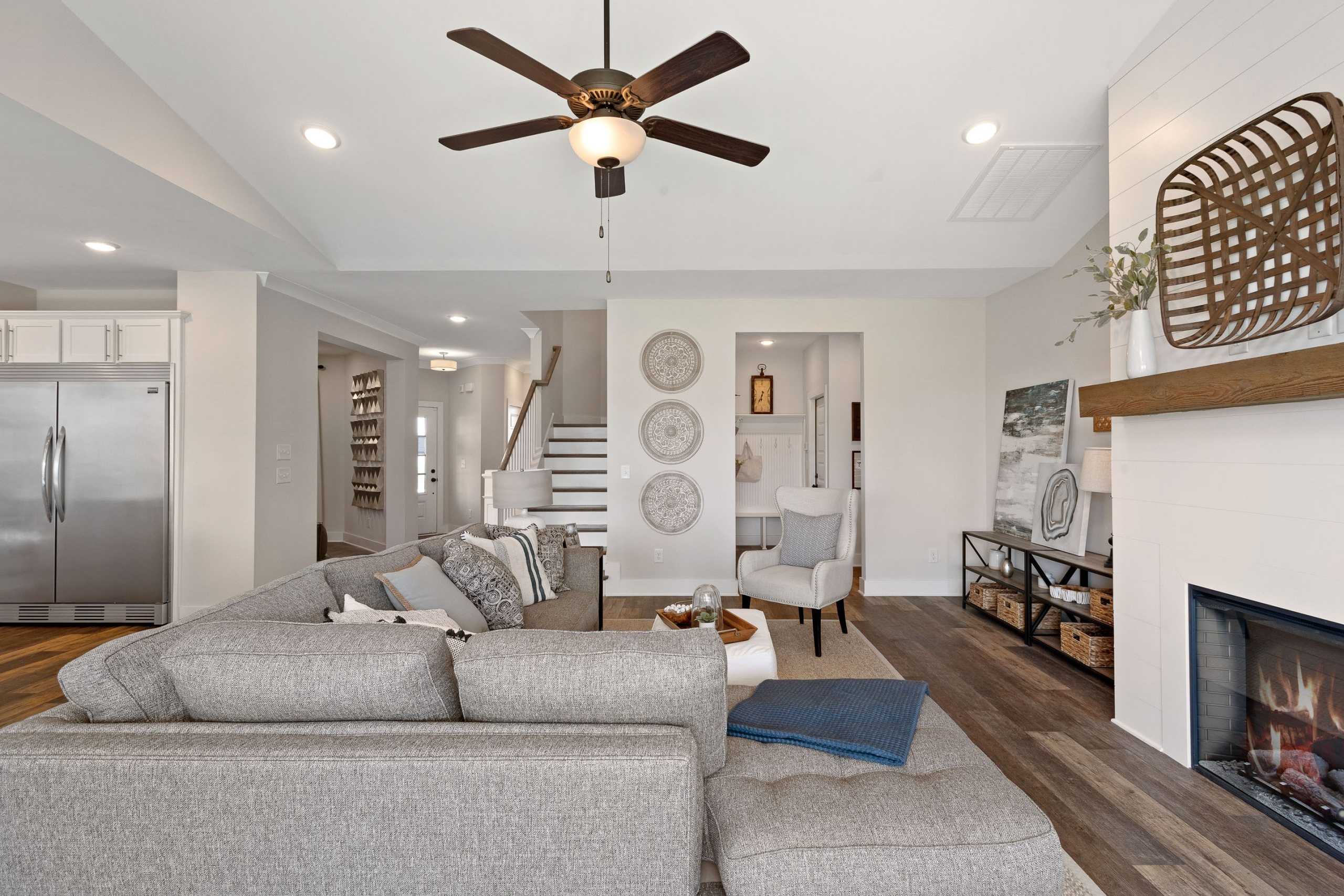 Spacious open-concept living room in Rivers Edge Murfreesboro TN with gray L-shaped sofa, gas fireplace, hardwood floors, and ceiling fan