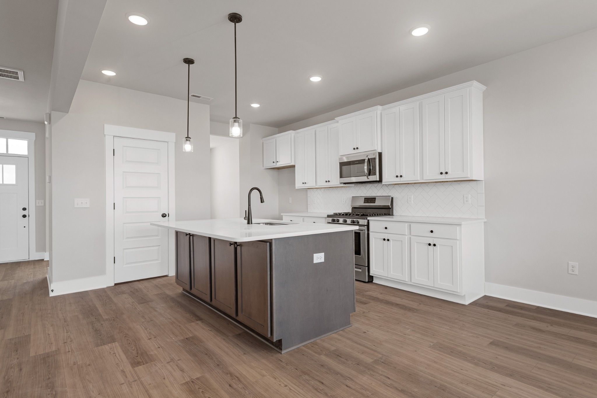 Modern kitchen with white cabinets, dark island, and stainless steel appliances in The Willow B plan at Calista Farms.