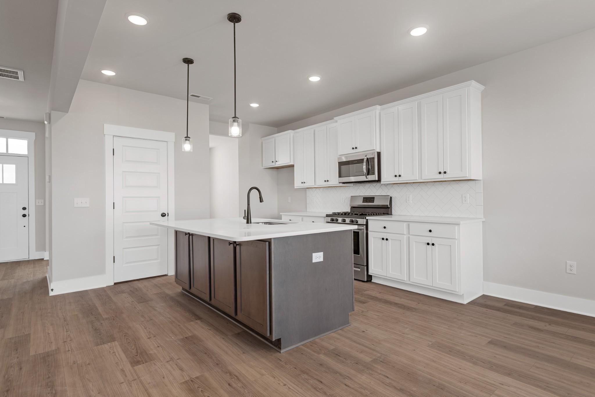 Modern kitchen with white cabinets, dark island, and stainless steel appliances in The Willow B plan at Calista Farms.