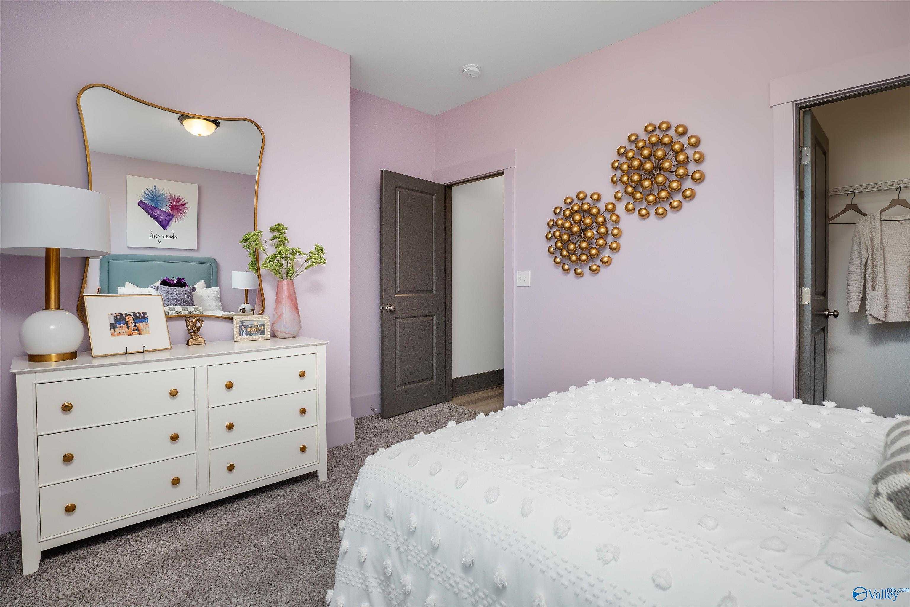 Cozy pink secondary bedroom with tufted white bed, gold mirror, dresser, and walk-in closet in Davidson Homes The Rockford B, Madison AL