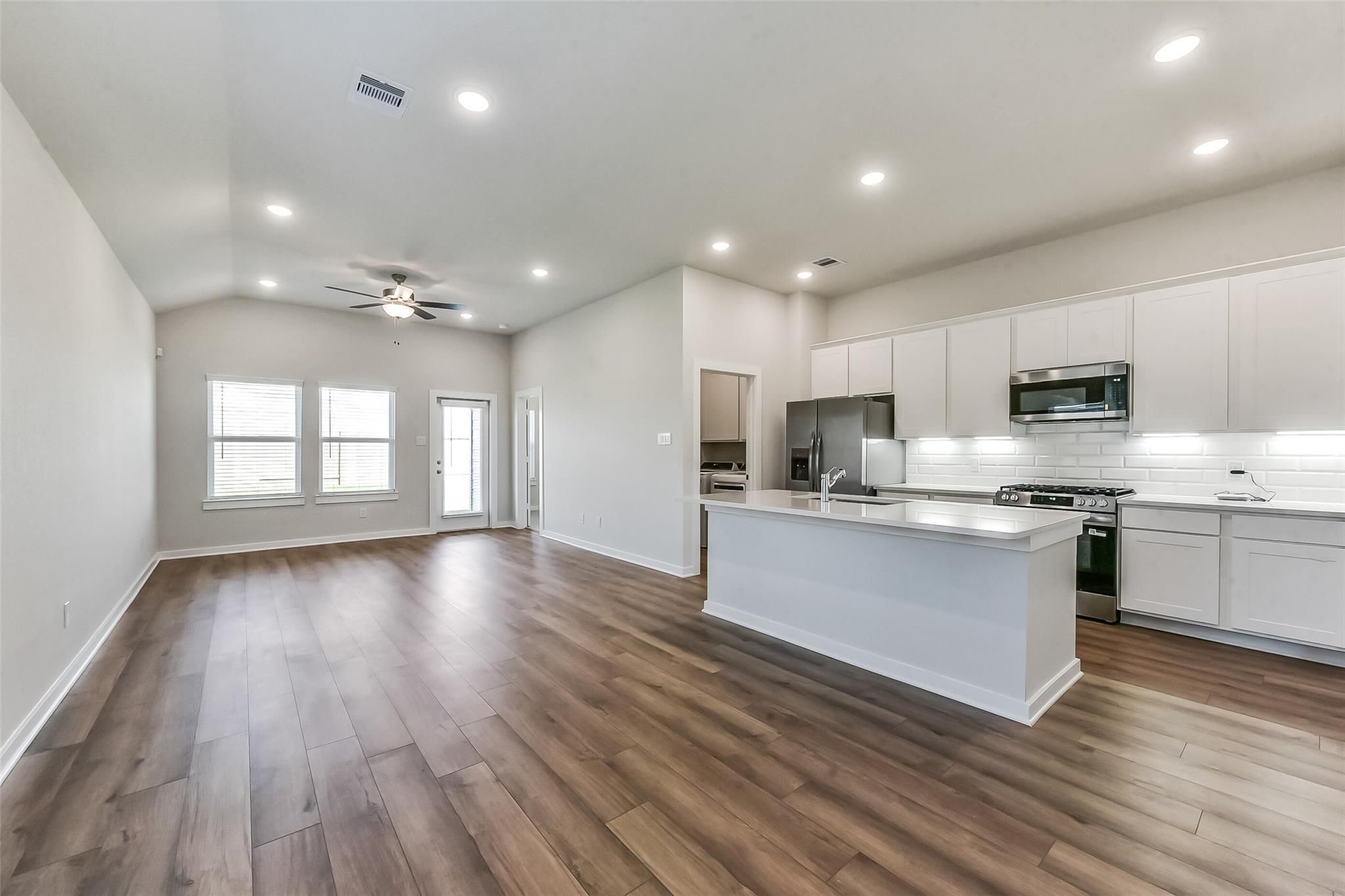Open-concept kitchen and living area with white cabinets, stainless appliances, quartz island, and hardwood floors in The Costa B home, Dayton TX
