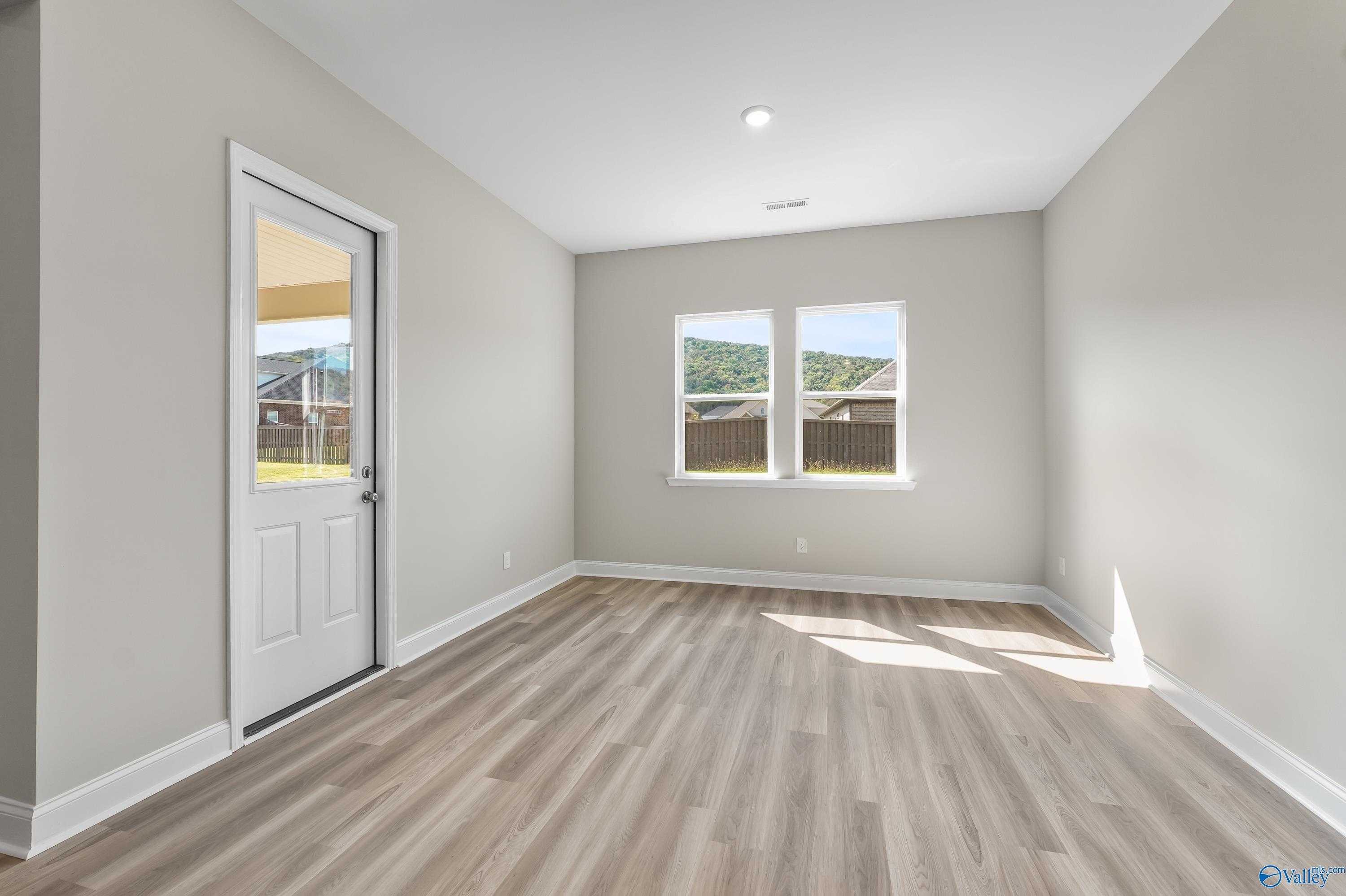 Bright secondary bedroom with light gray walls, light wood floors, glass-paneled door, and hill-view windows in Evermore Homes The Haven, Owens Cross Roads