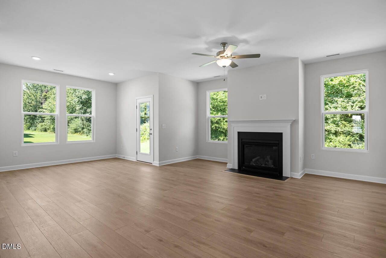 Bright great room with hardwood floors, fireplace, ceiling fan, and large windows in The Daphne D by Davidson Homes, Zebulon NC