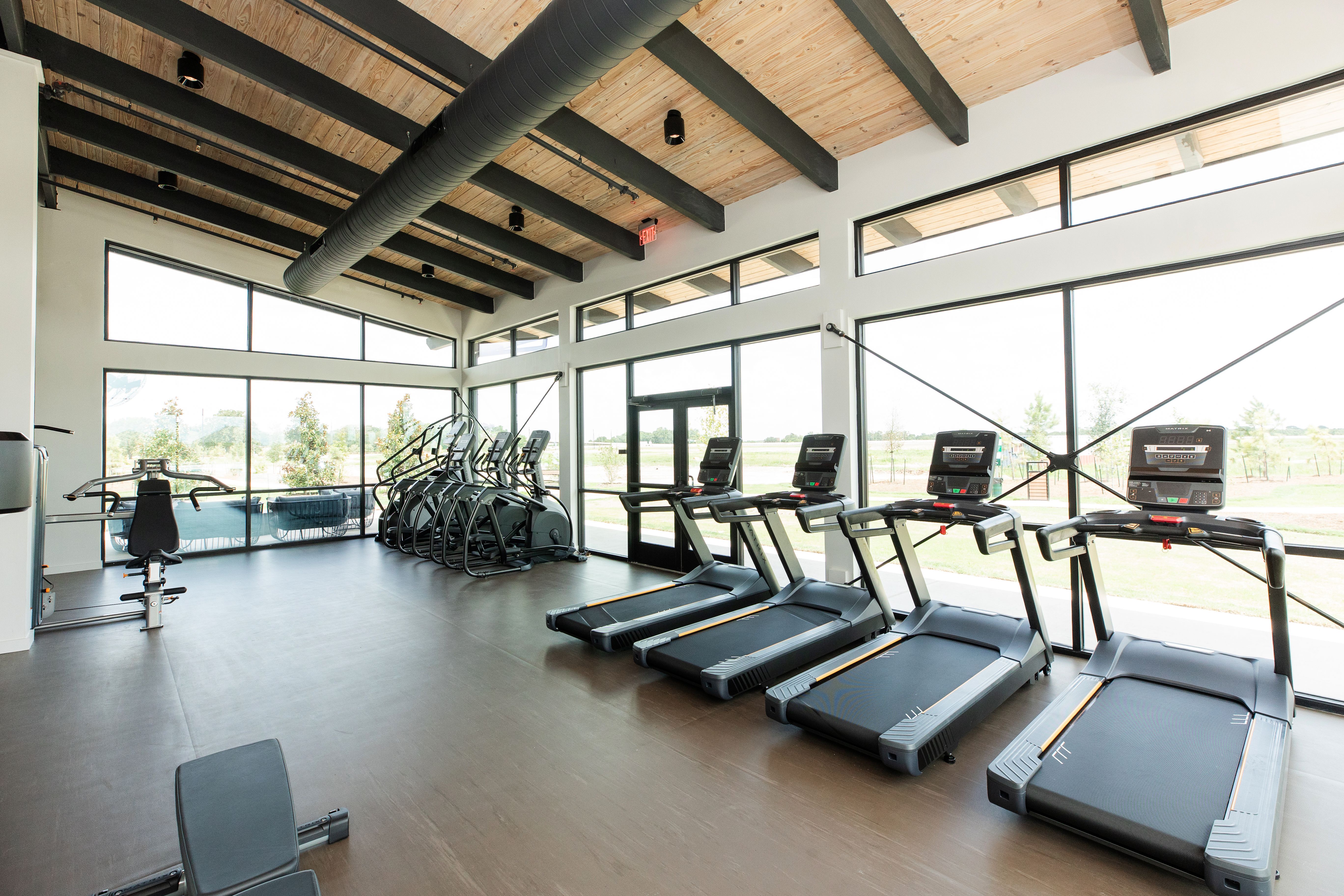 Spacious fitness center at Emberly in Beasley Texas featuring treadmills bikes weights wooden beams and large windows