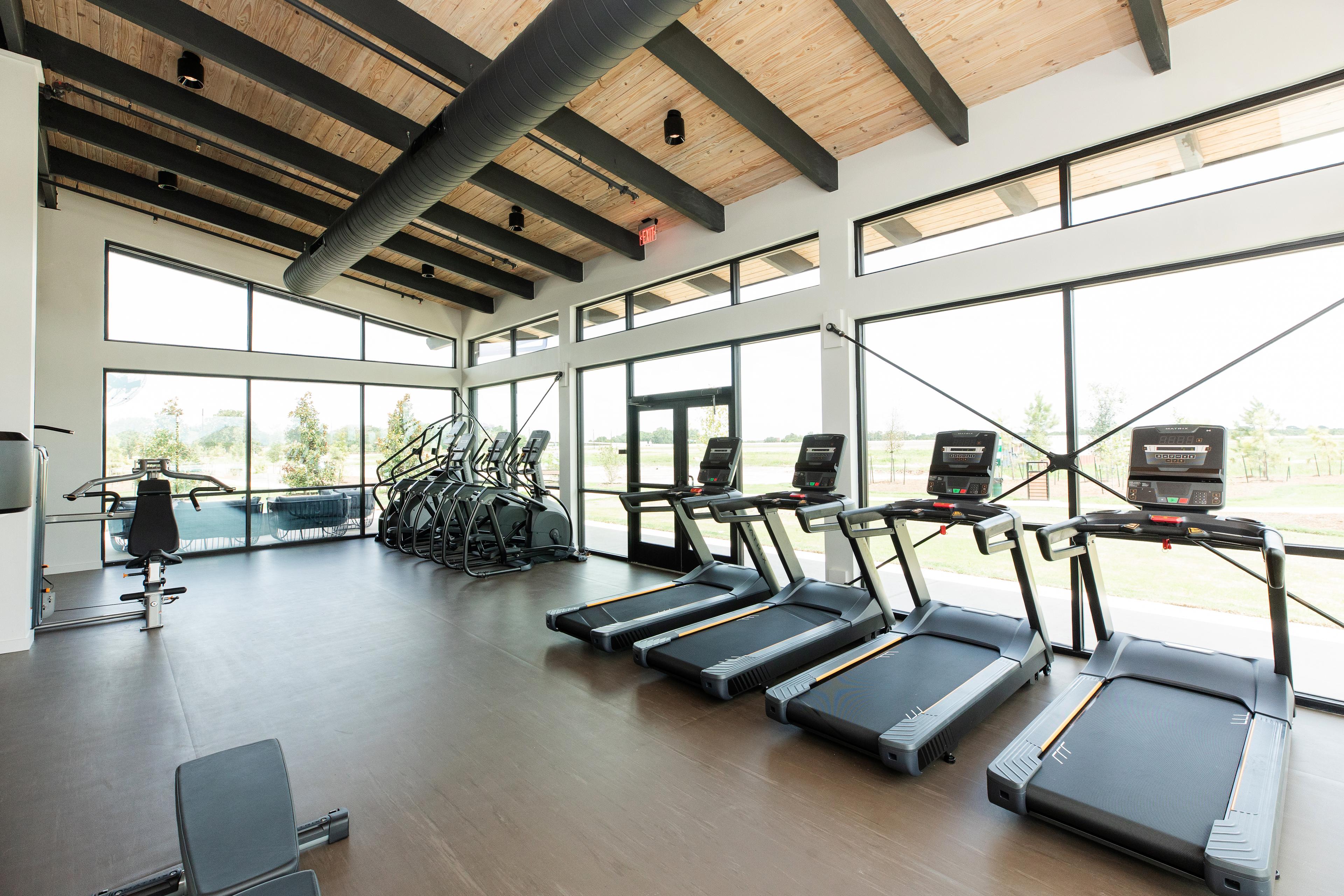 Spacious fitness center at Emberly in Beasley Texas featuring treadmills bikes weights wooden beams and large windows