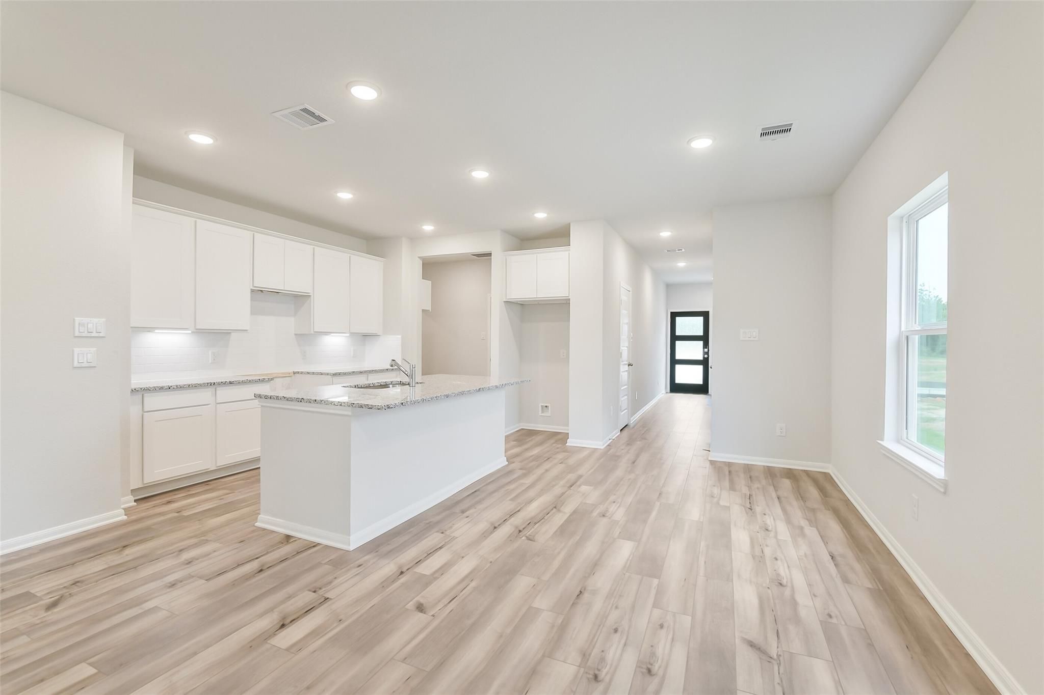 Modern white kitchen with large island sink, cabinets, hardwood floors opening to hallway in Davidson Homes Brazos F, Conroe TX