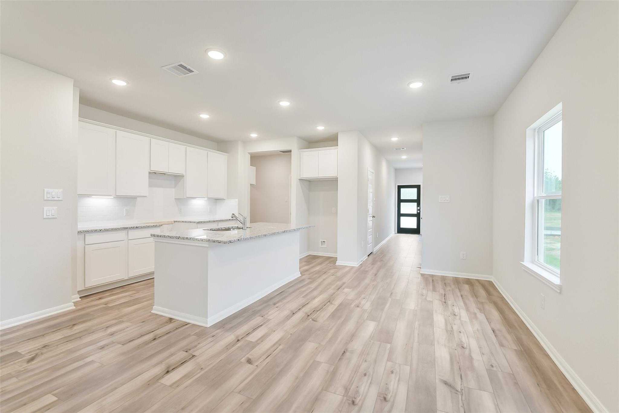 Modern white kitchen with large island sink, cabinets, hardwood floors opening to hallway in Davidson Homes Brazos F, Conroe TX