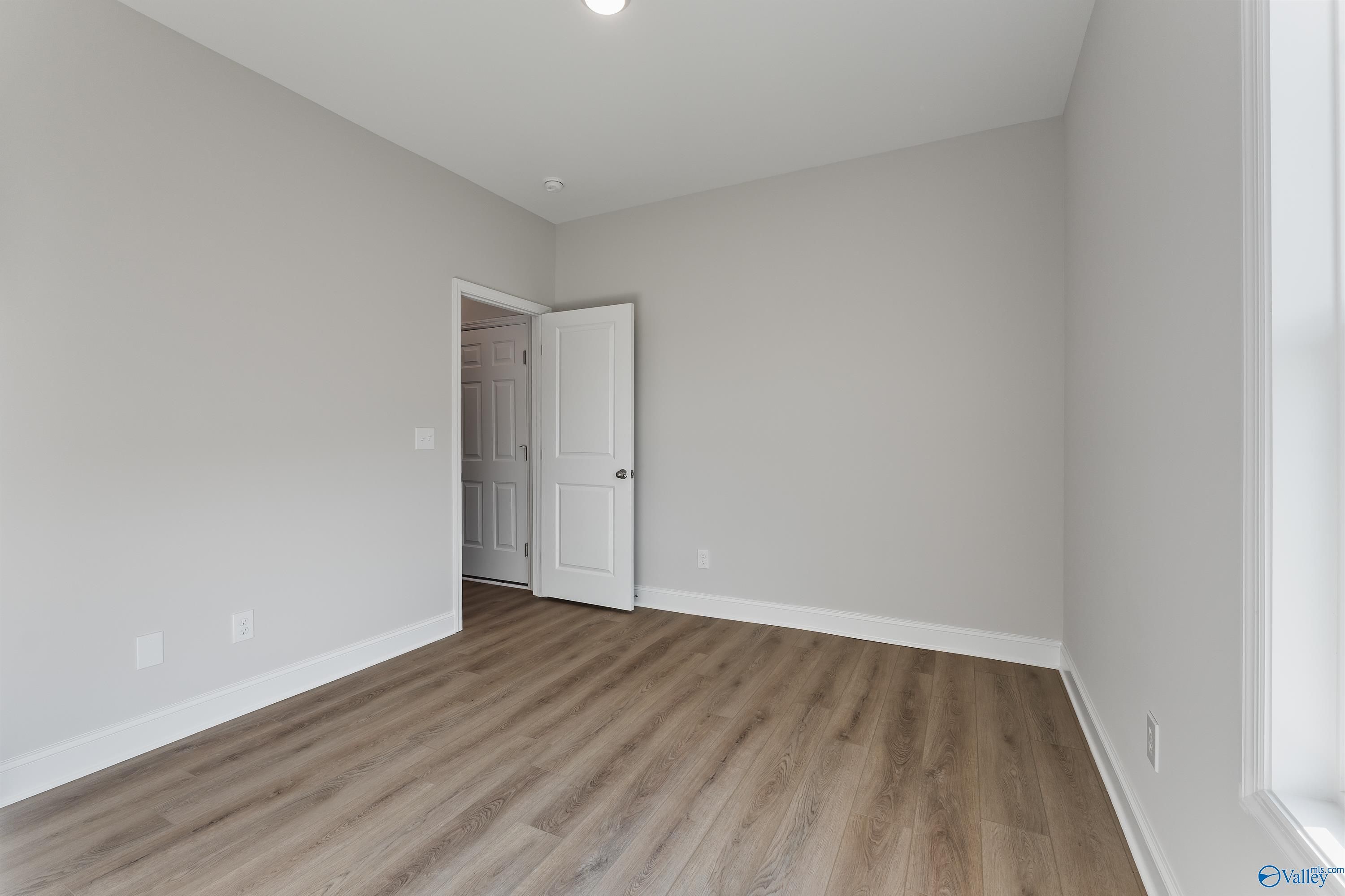 Spacious empty bedroom with light gray walls, white door, and laminate wood flooring in Davidson Homes The Daphne, Hazel Green, Alabama