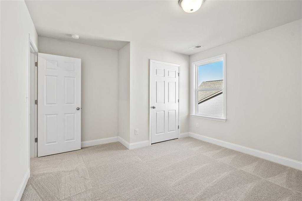 Bright secondary bedroom with neutral walls, plush carpet, double doors, and window in Davidson Homes The Ash C, Wehunt Meadows, Hoschton