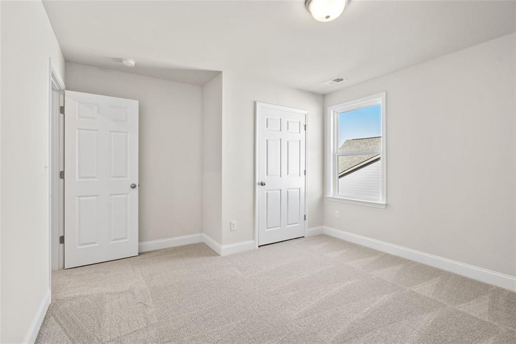 Bright secondary bedroom with neutral walls, plush carpet, double doors, and window in Davidson Homes The Ash C, Wehunt Meadows, Hoschton