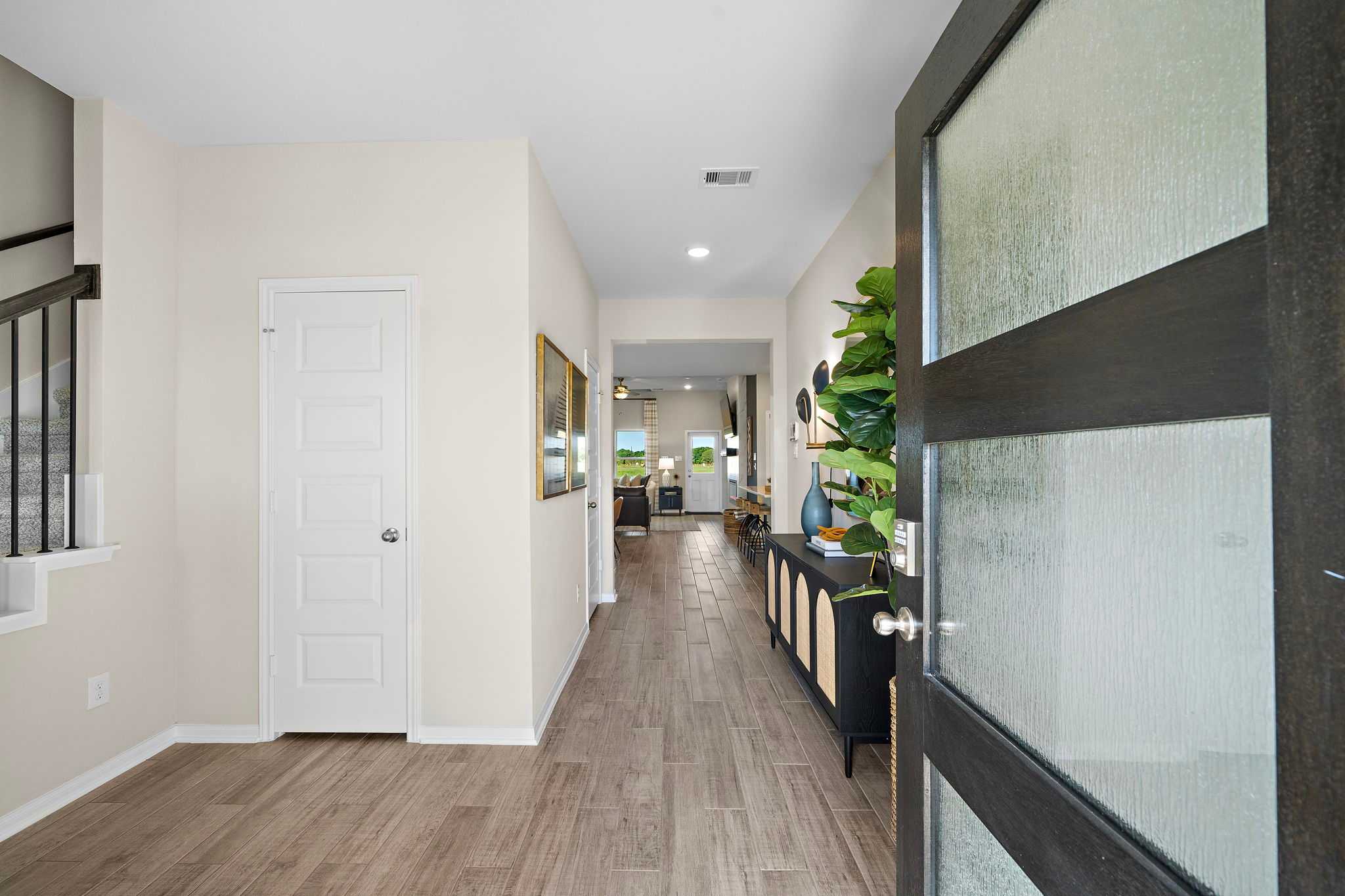 Spacious entryway hallway in Emberly Beasley Texas home with light hardwood floors frosted glass door and potted plants