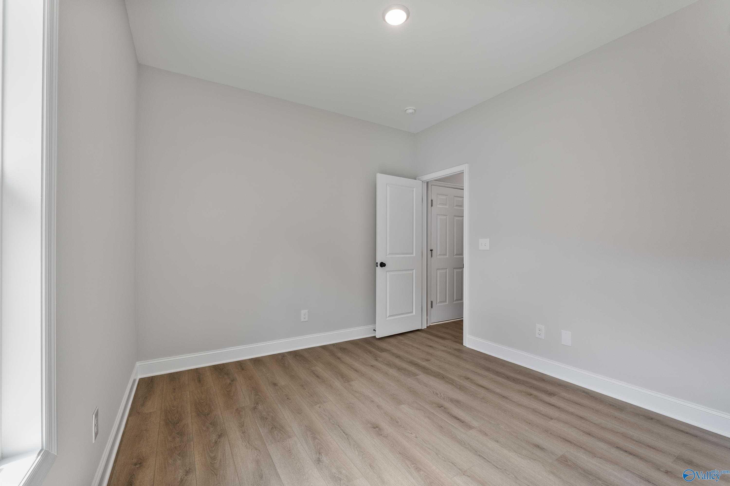 Bright secondary bedroom with gray walls, laminate wood floors, and window in Davidson Homes The Daphne, Huntsville AL