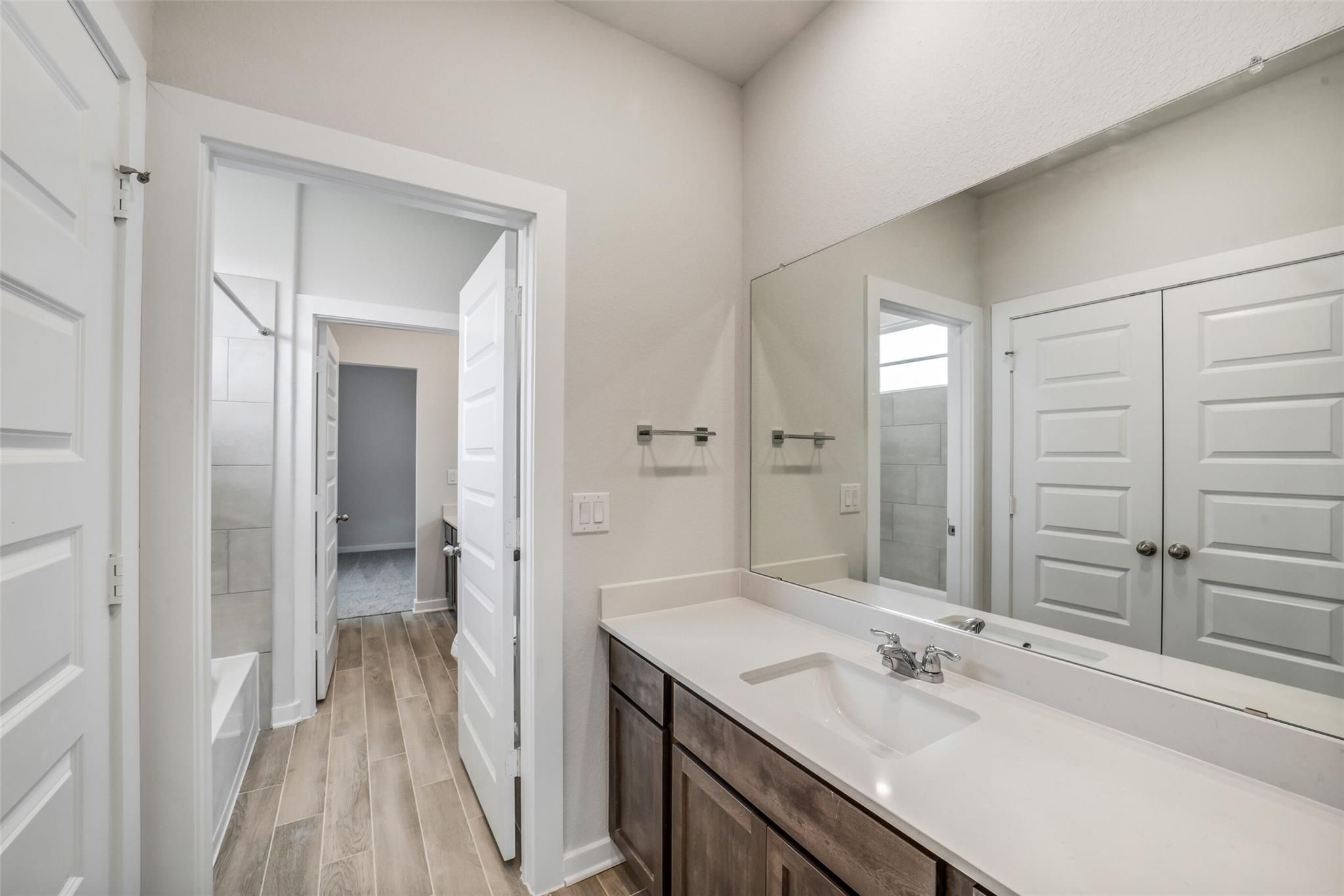Elegant guest bathroom with quartz vanity, large mirror, subway tile tub, and wood floors in Davidson Homes Acadia C, Magnolia TX