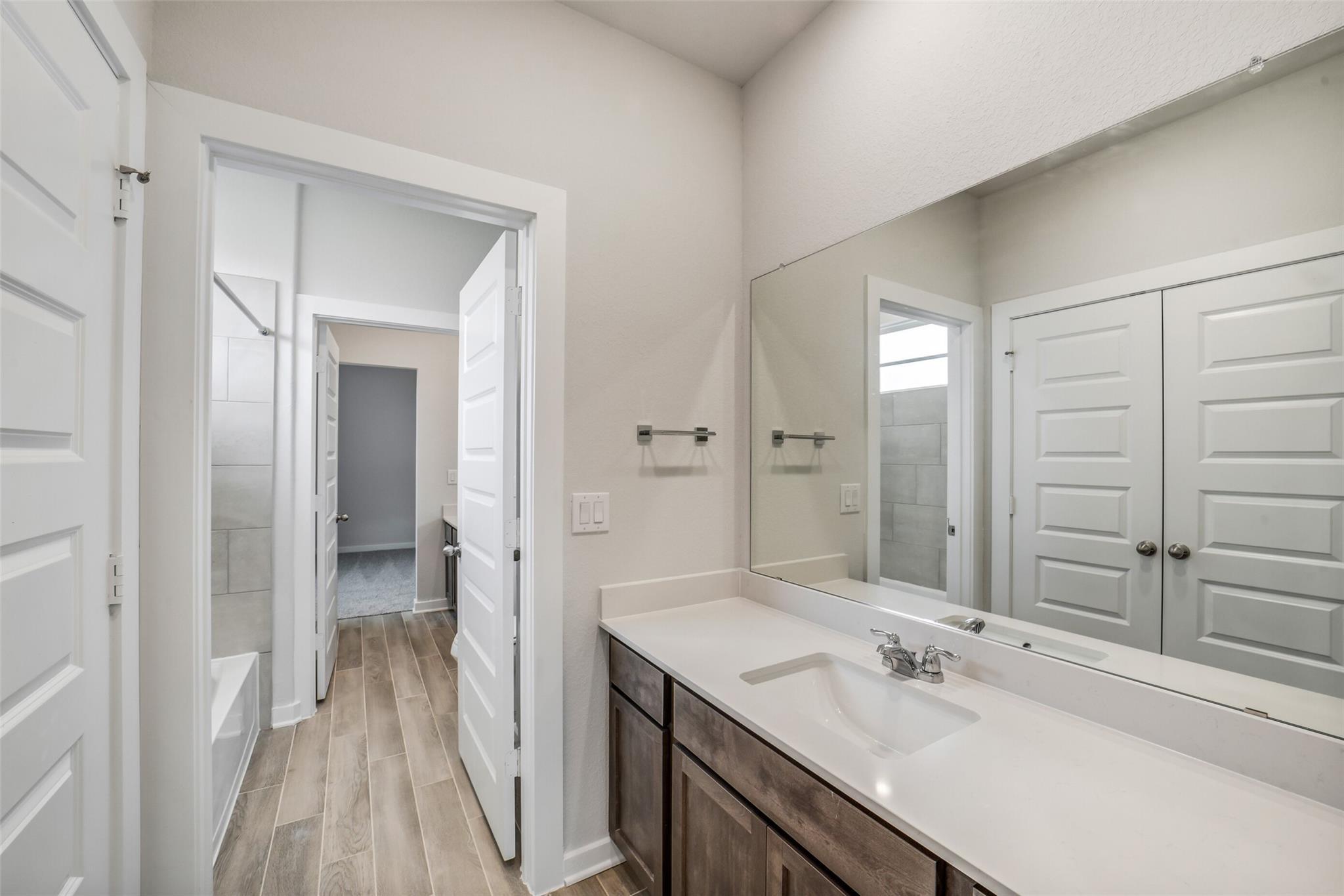 Elegant guest bathroom with quartz vanity, large mirror, subway tile tub, and wood floors in Davidson Homes Acadia C, Magnolia TX