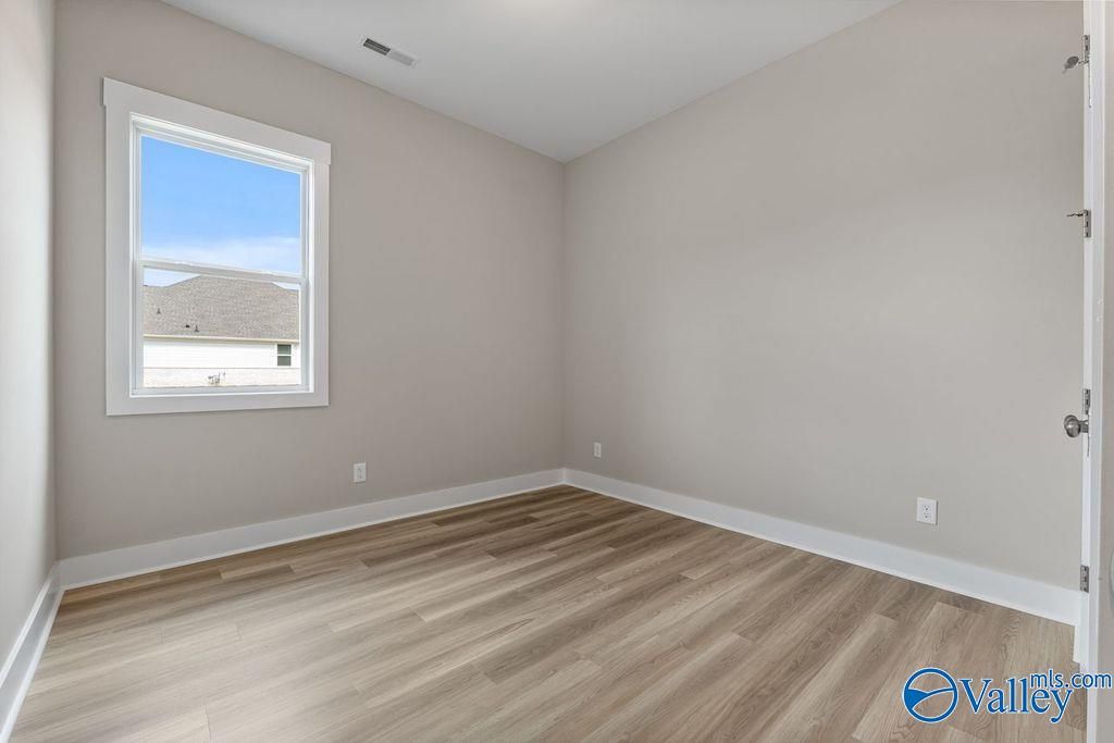 Empty secondary bedroom featuring light gray walls, large window, and hardwood-look flooring in Evermore Homes The Oxford, Owens Cross Roads, AL