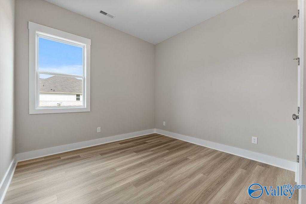 Bright empty bedroom with light gray walls, hardwood laminate floors, and large window overlooking neighborhood in The Oxford home, Owens Cross Roads, AL