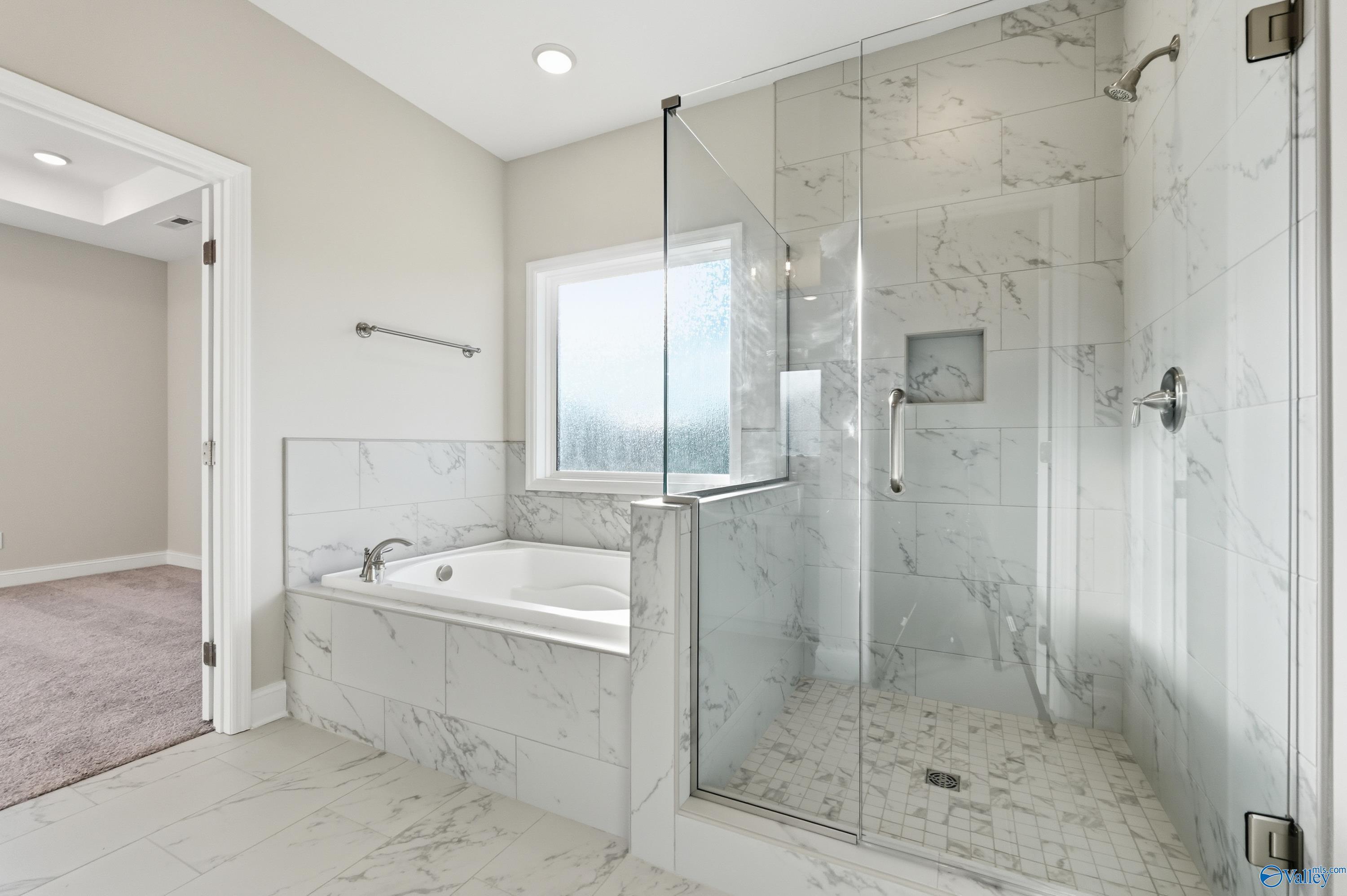 Elegant master bathroom with freestanding tub, frameless glass shower, and white marble tiles in Davidson Homes The Montgomery B, Toney, Alabama