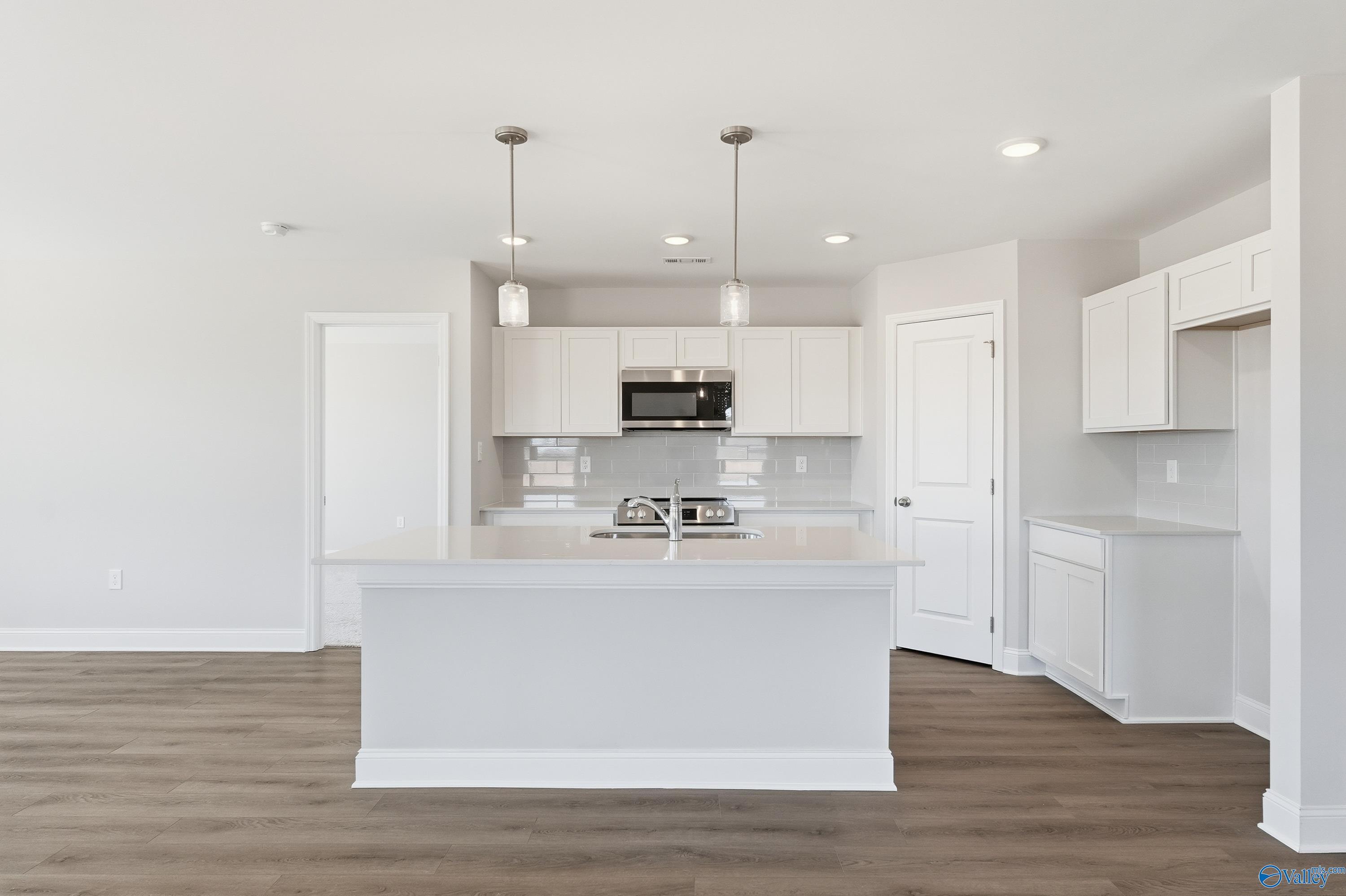 Modern white kitchen with island sink, stainless microwave, dishwasher, and pendant lights in Davidson Homes The Franklin, New Market, Alabama