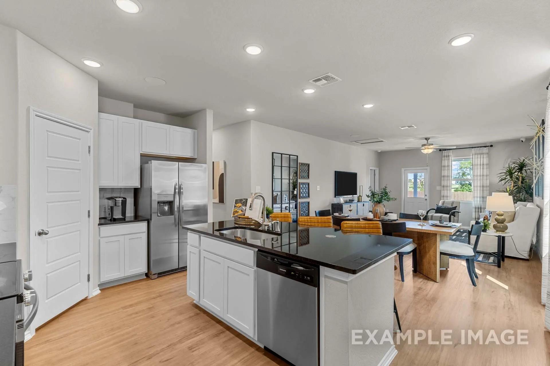 Open-concept kitchen with white cabinets and black granite island in The Sabine H floor plan at Heartland, Texas.