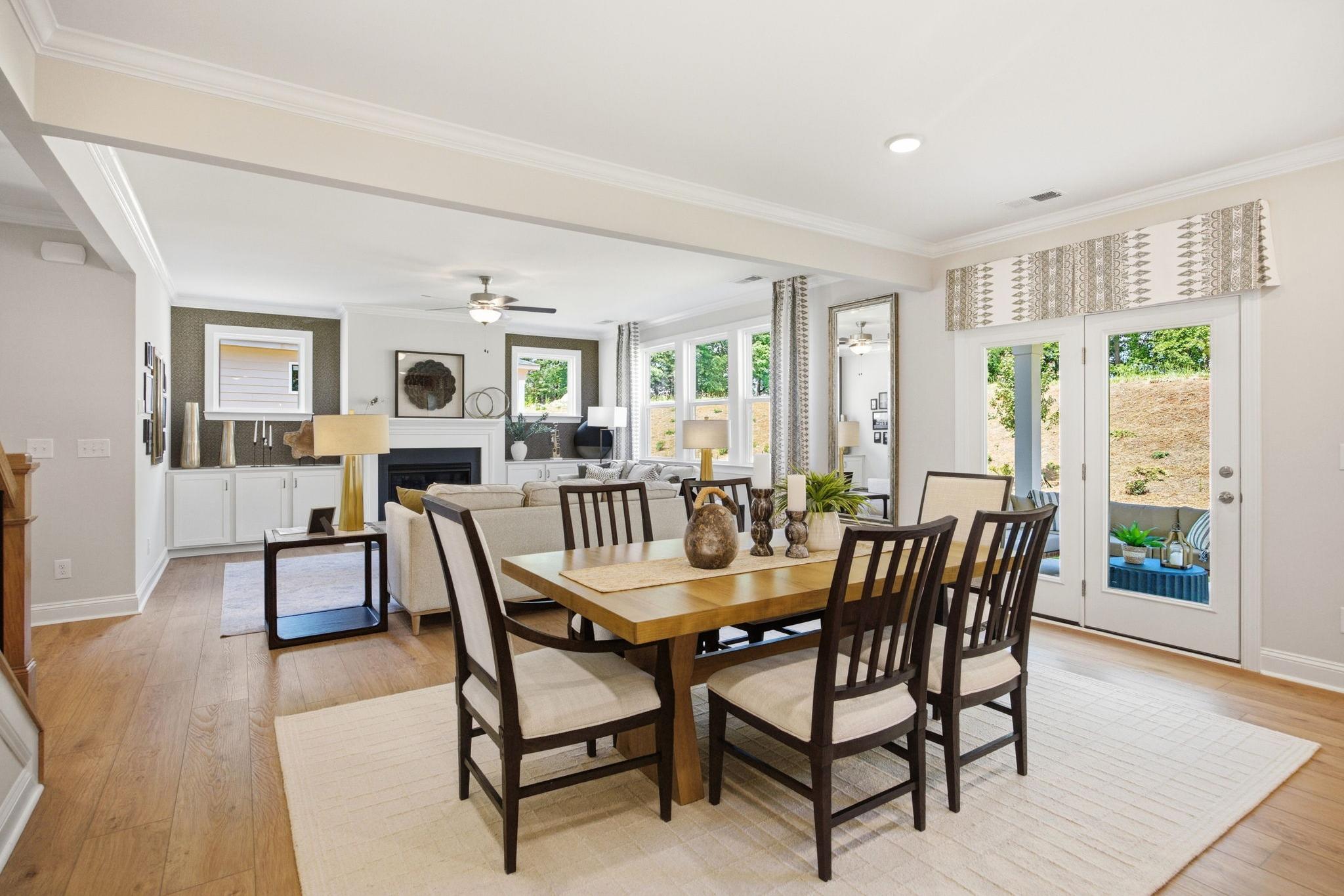 Open-concept dining and living room at Enclave at Belmont in Belmont NC with hardwood floors, wooden table, fireplace, and sliding doors