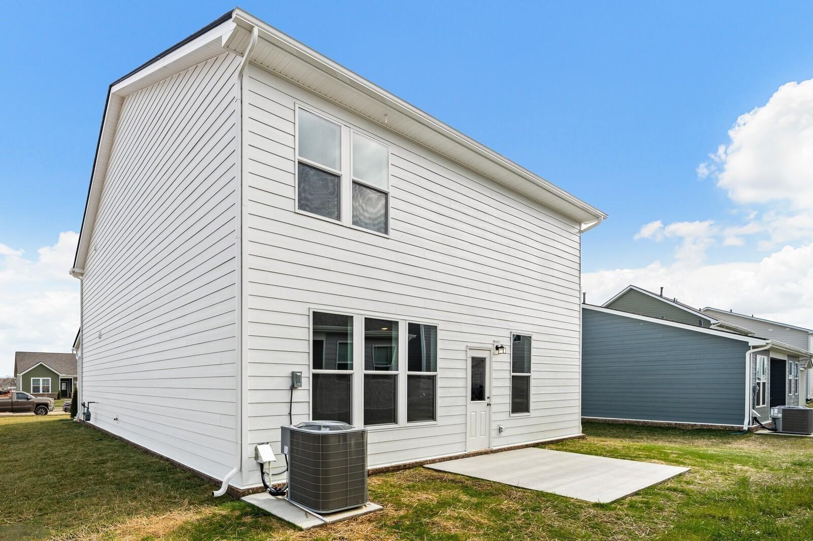 Two-story white clapboard home exterior with large windows, back door, concrete patio, and AC unit in Sage Farms, White House, TN - Davidson Homes The Logan C