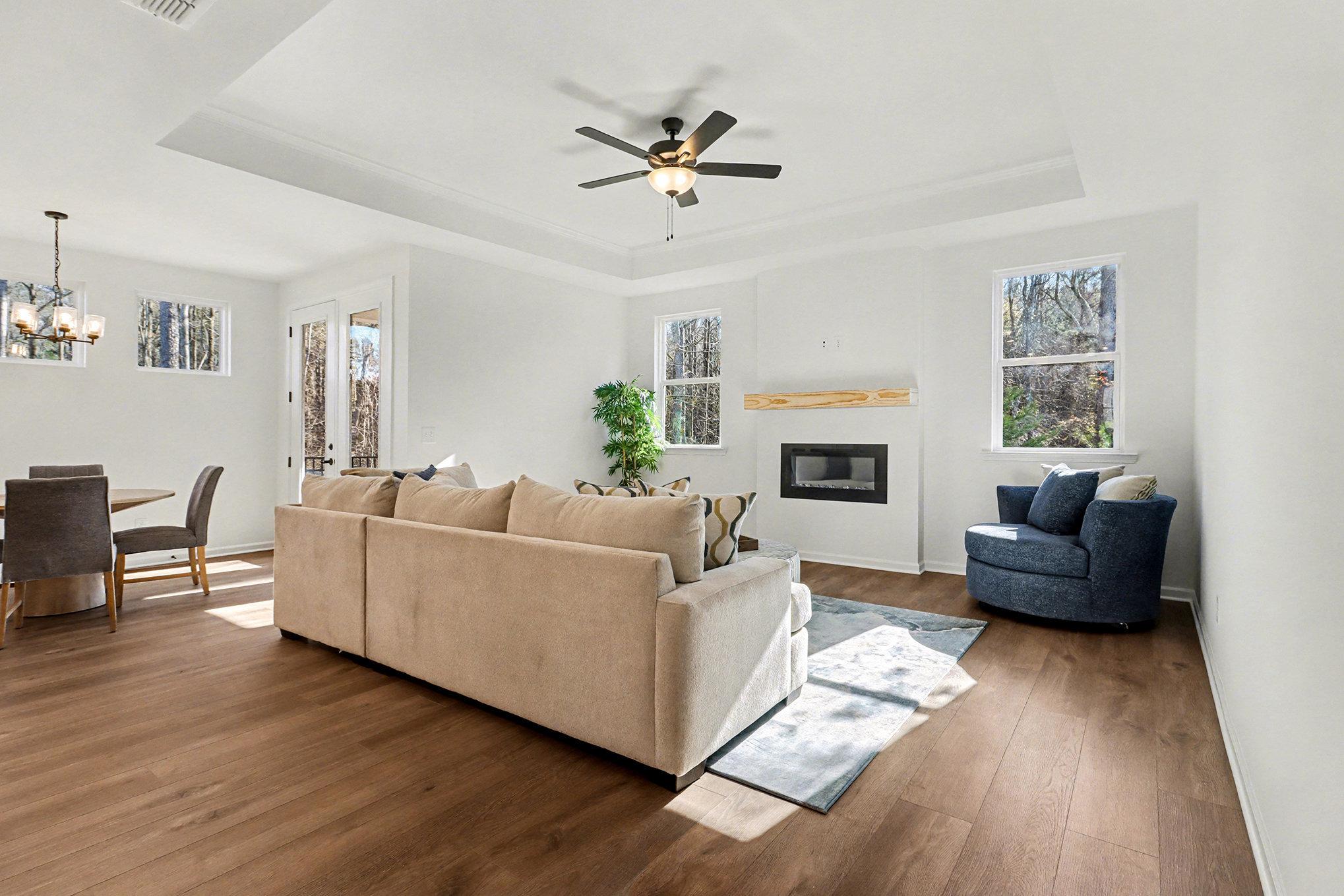 Cozy modern living room with gray sectional sofa, blue armchair, electric fireplace, and open kitchen in The Daphne B 4-bedroom home, Loganville, Georgia