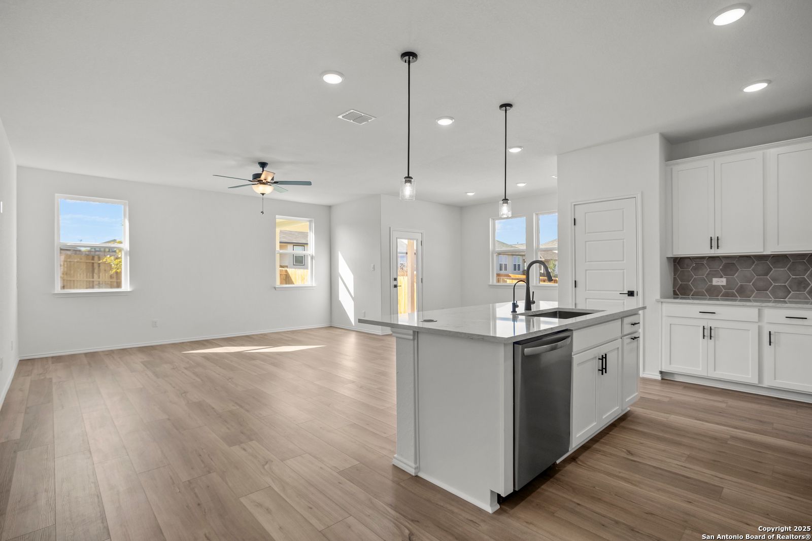 Modern open-concept kitchen with white shaker cabinets, quartz island, stainless dishwasher, and luxury vinyl plank floors in Davidson Homes The Daphne K, San Antonio