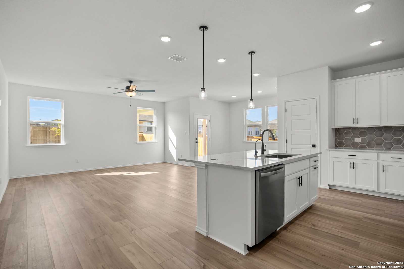 Modern open-concept kitchen with white shaker cabinets, quartz island, stainless dishwasher, and luxury vinyl plank floors in Davidson Homes The Daphne K, San Antonio