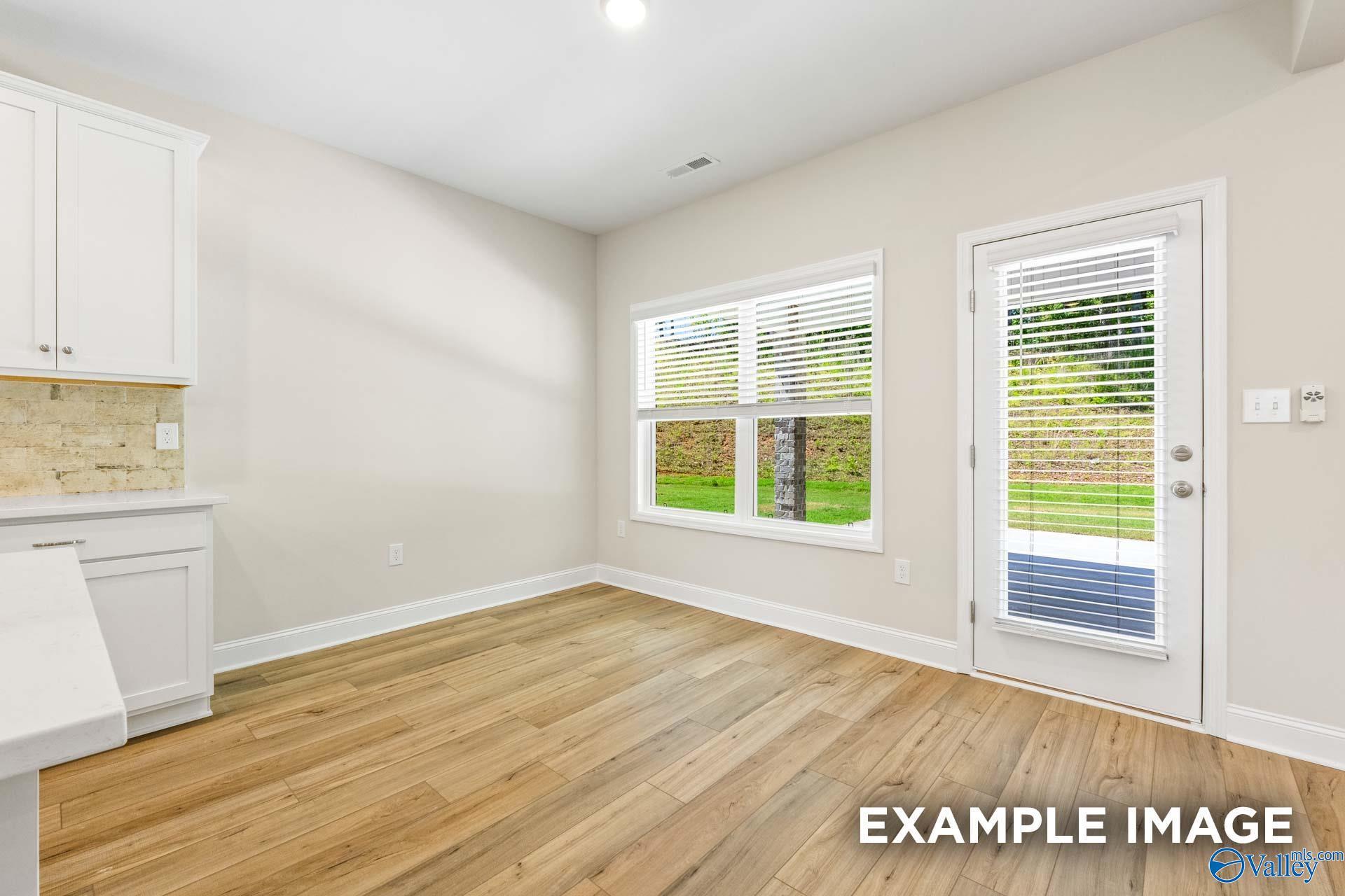 Bright room with white cabinets, quartz countertop, beige tile backsplash, hardwood floors, and backyard view through window and door in The Shelby B, Arab, AL