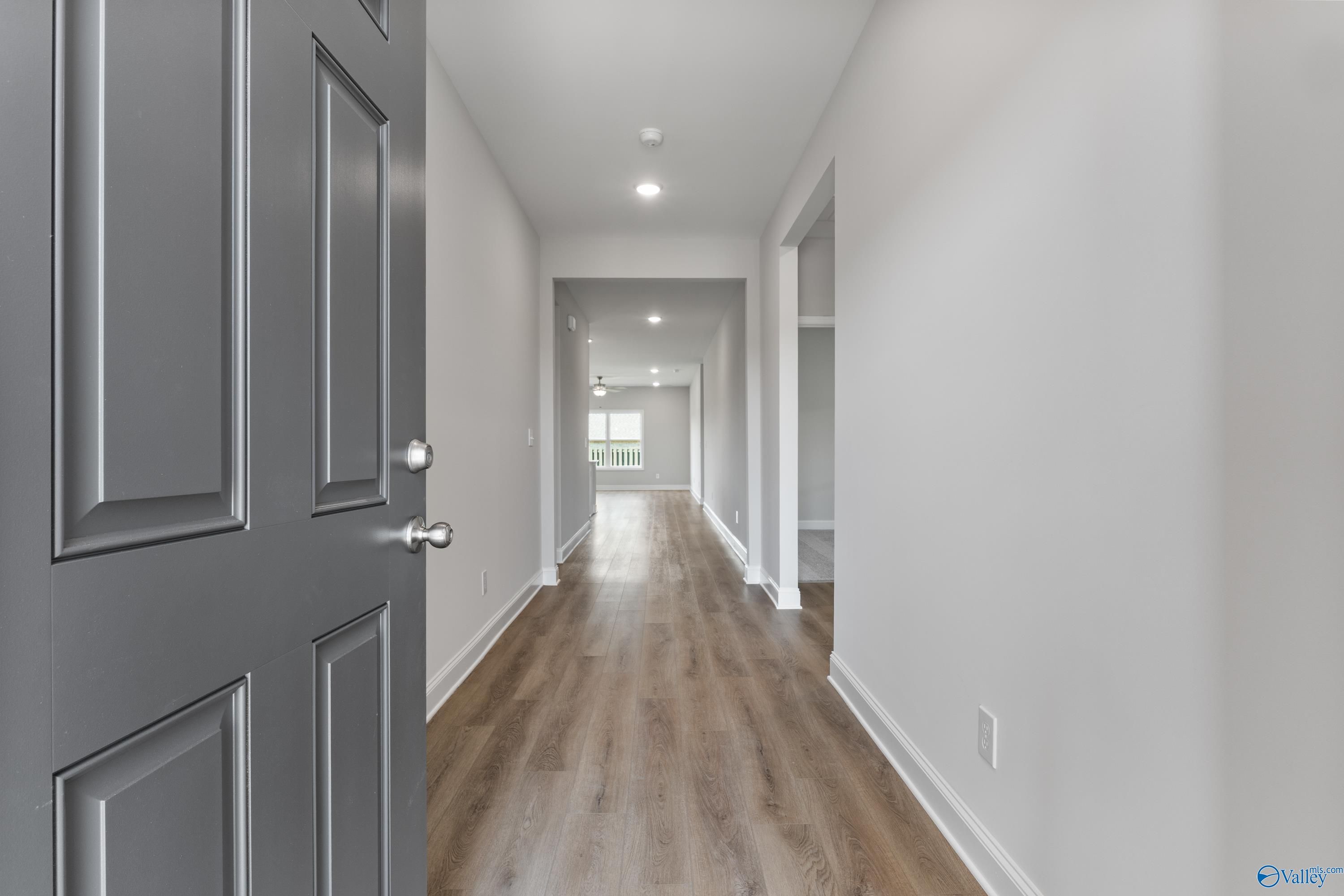 Wide hallway with hardwood floors, recessed lighting, and open doors in The Daphne 4-bedroom home, Hazel Green, Alabama