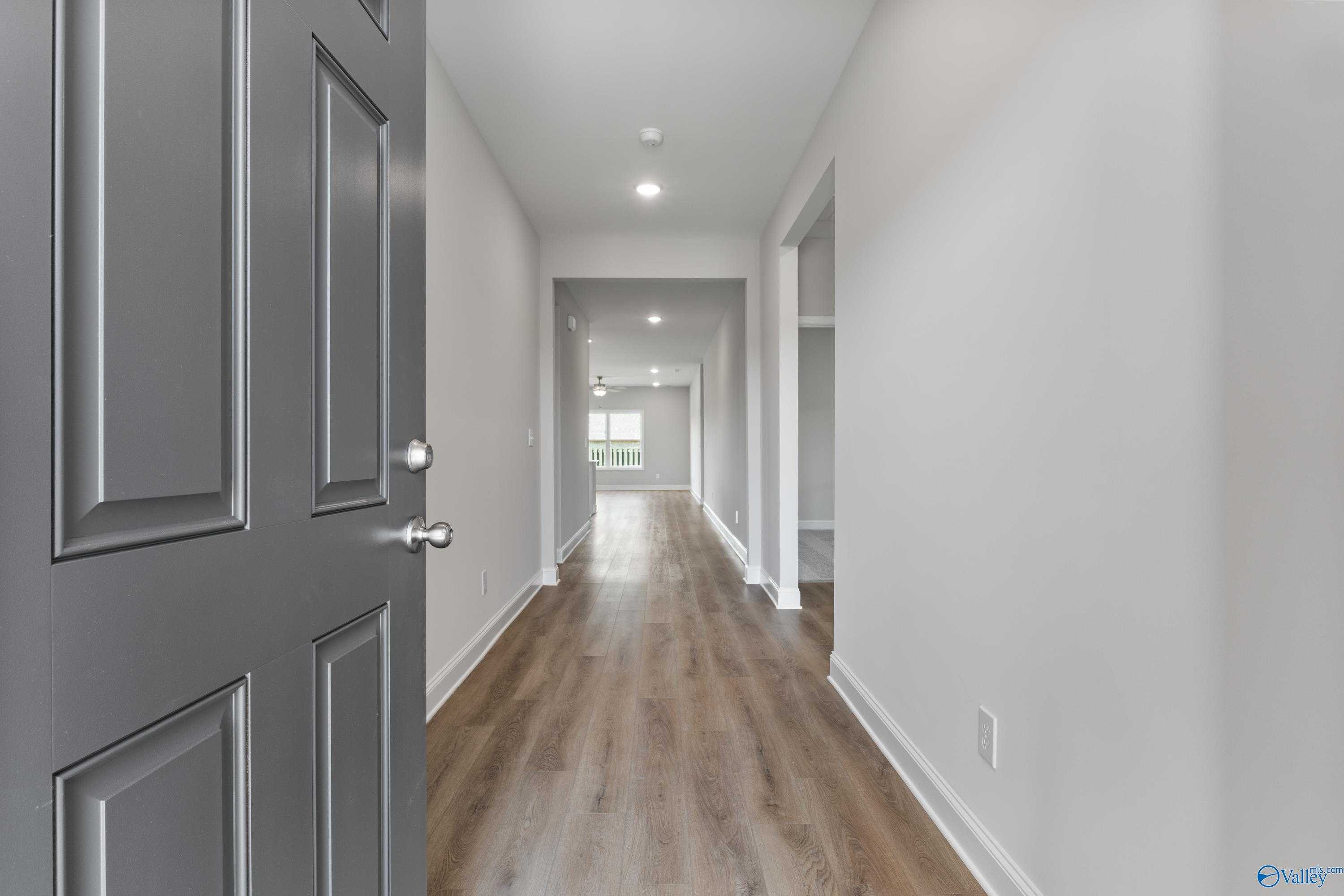 Wide hallway with hardwood floors, recessed lighting, and open doors in The Daphne 4-bedroom home, Hazel Green, Alabama