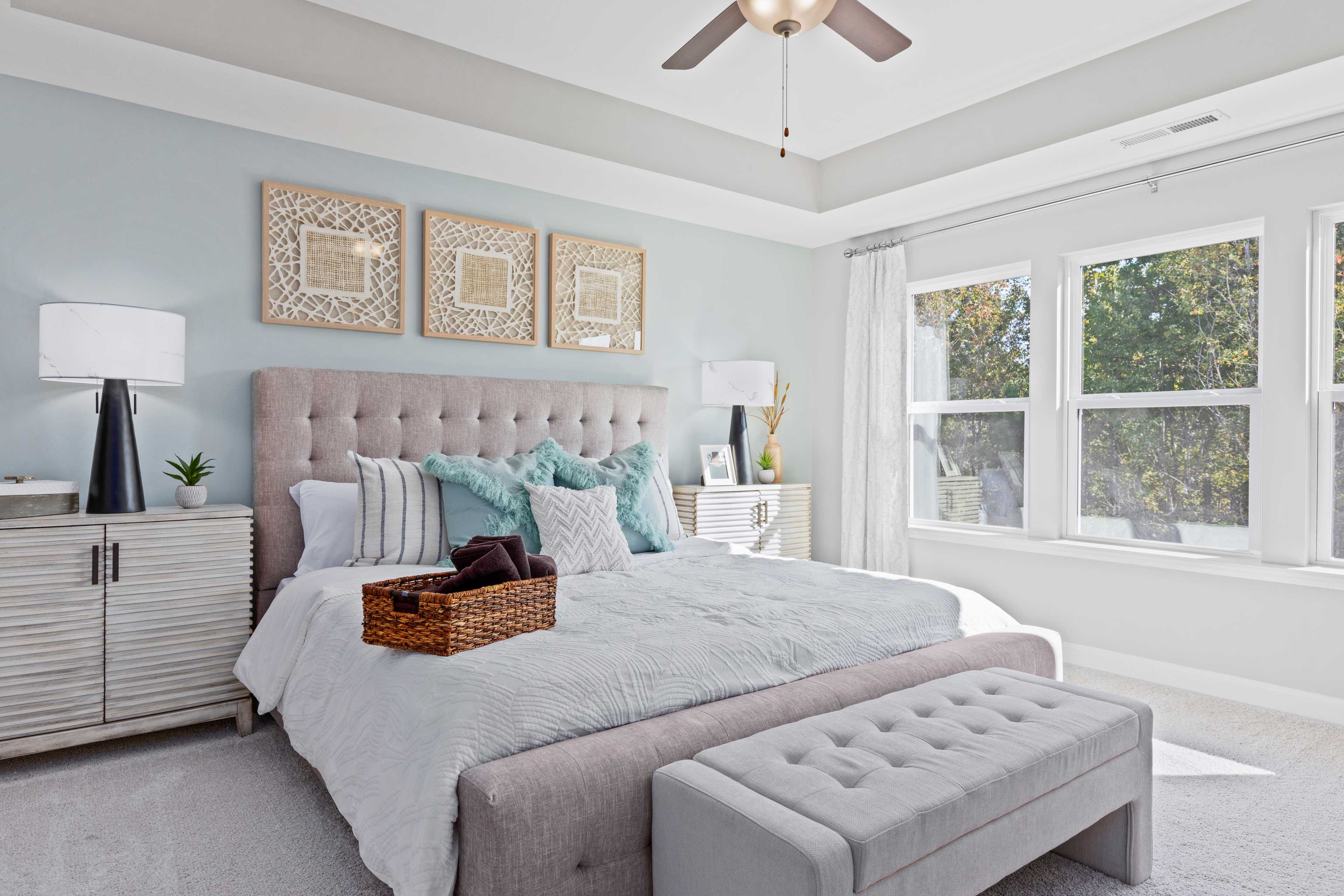 Serene primary bedroom at Enclave at Belmont in Belmont NC with tufted bed, teal pillows, and large windows