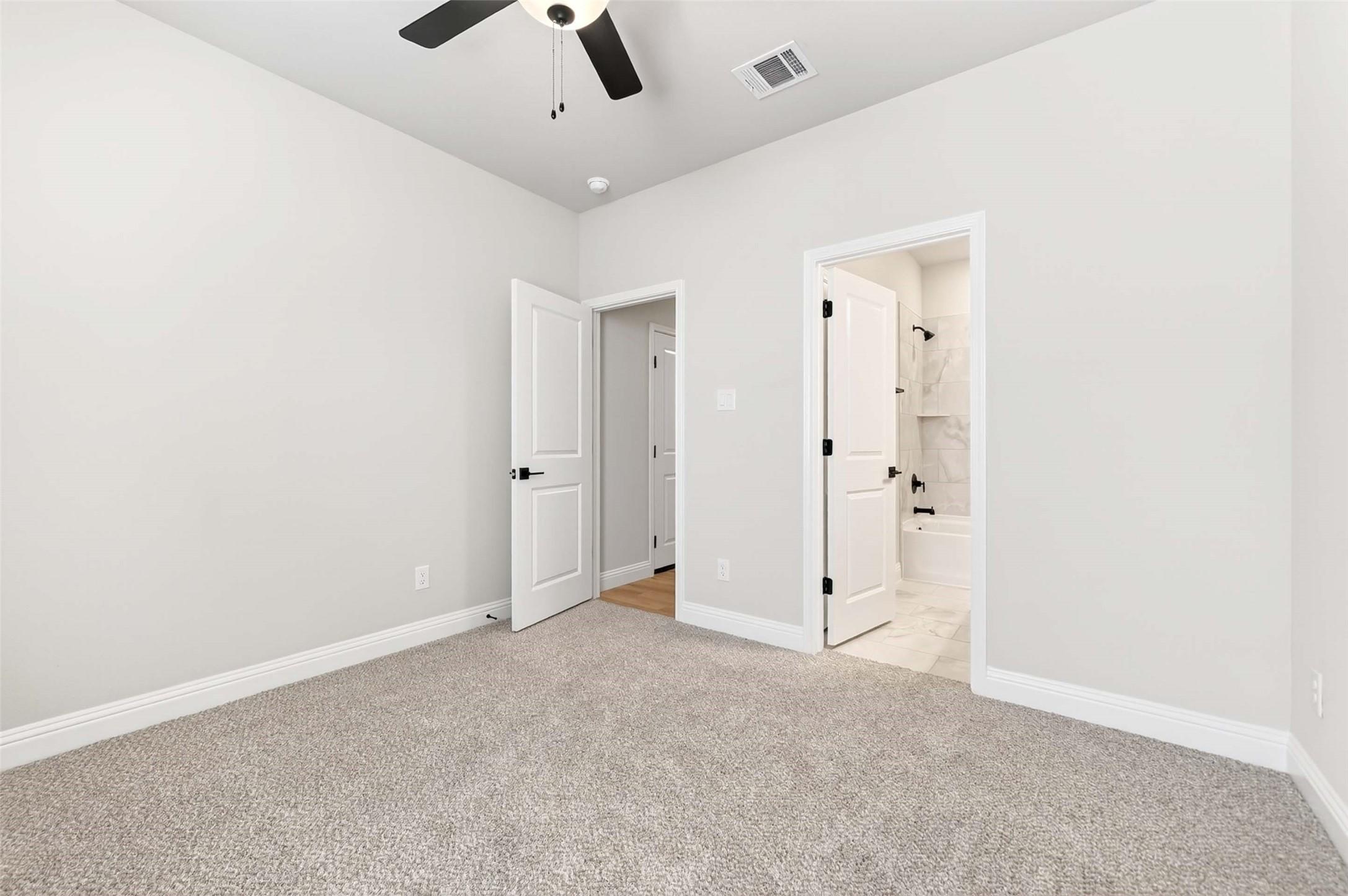Secondary bedroom with plush carpet and en-suite bath in The Holly C floor plan by Davidson Homes in Anna, Texas.