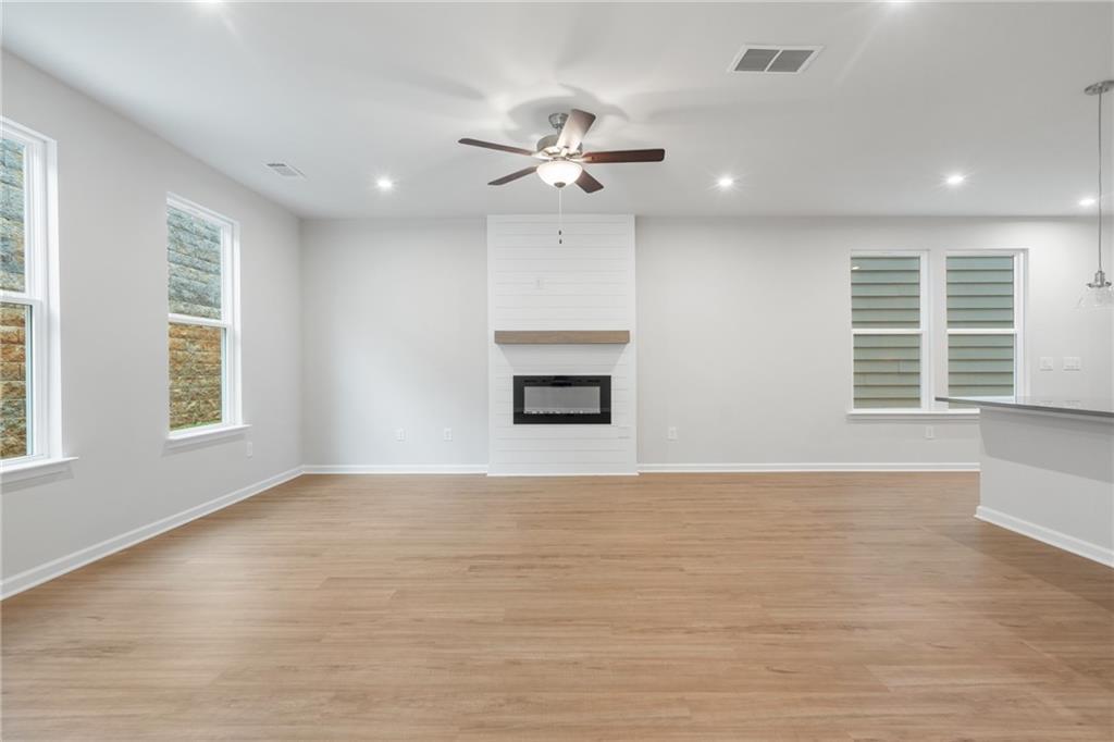 Spacious living room with modern gas fireplace, hardwood floors, ceiling fan, and large windows in Davidson Homes The Cary A, Kennesaw, GA