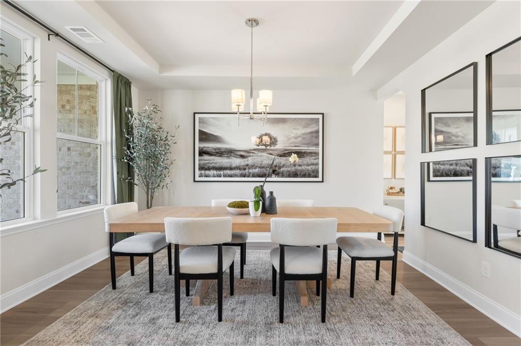 Elegant dining room with rectangular wood table, white upholstered chairs, chandelier, and large black-and-white artwork in The Danbury C by Davidson Homes, Buford, Georgia