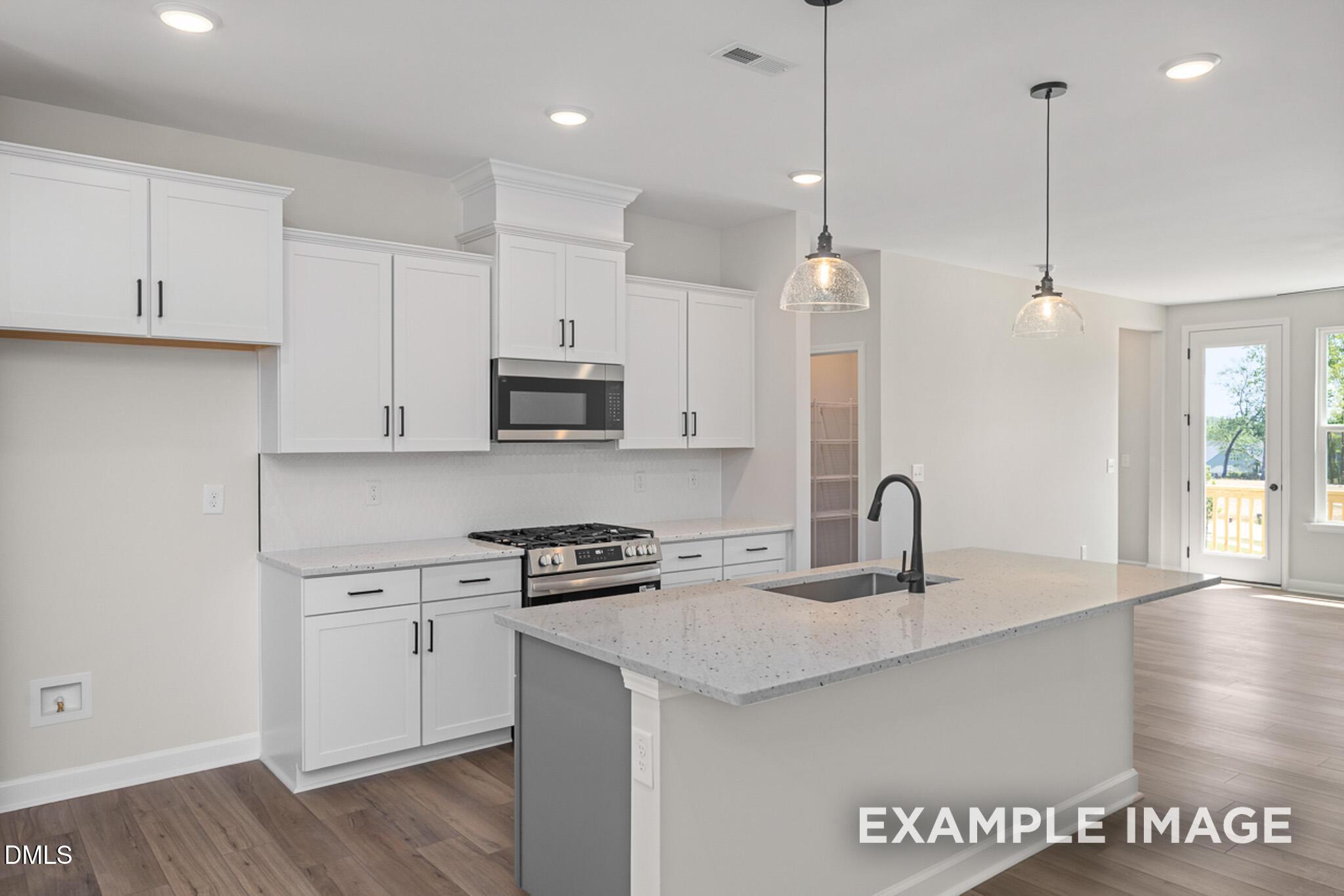Modern kitchen with white cabinets, quartz island, and stainless appliances in The Mitchell floor plan, Camden Park, NC.