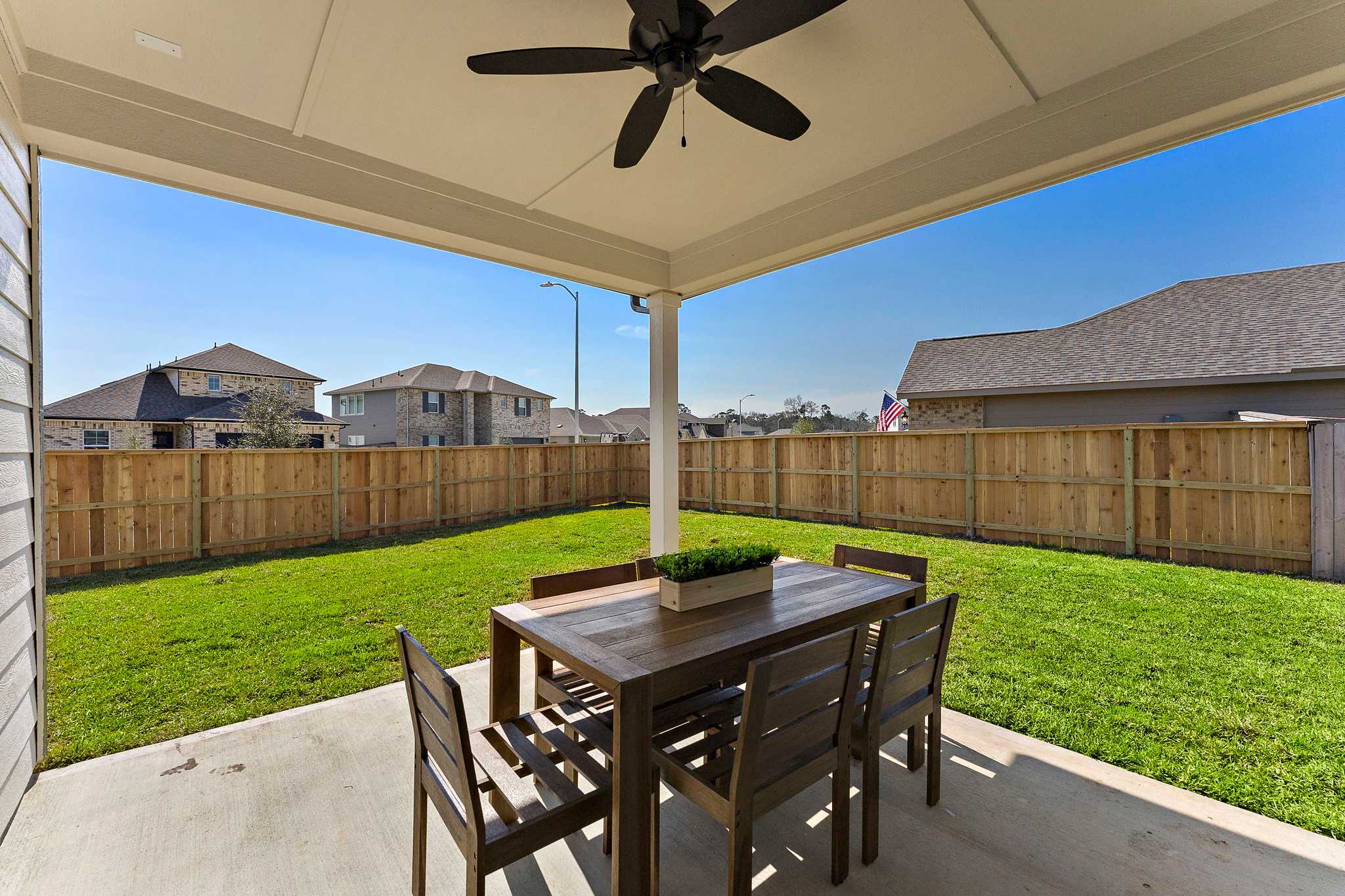 Covered patio at Sundance Cove in Crosby Texas with wooden dining table, chairs, ceiling fan, green lawn and privacy fence